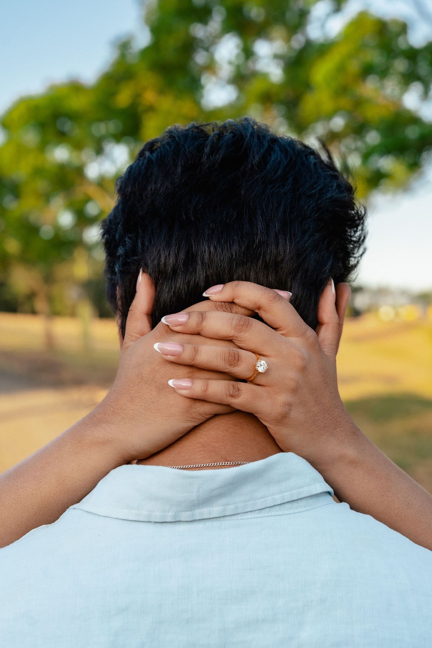Close-up view of hands covering the back of someone's neck outdoors.