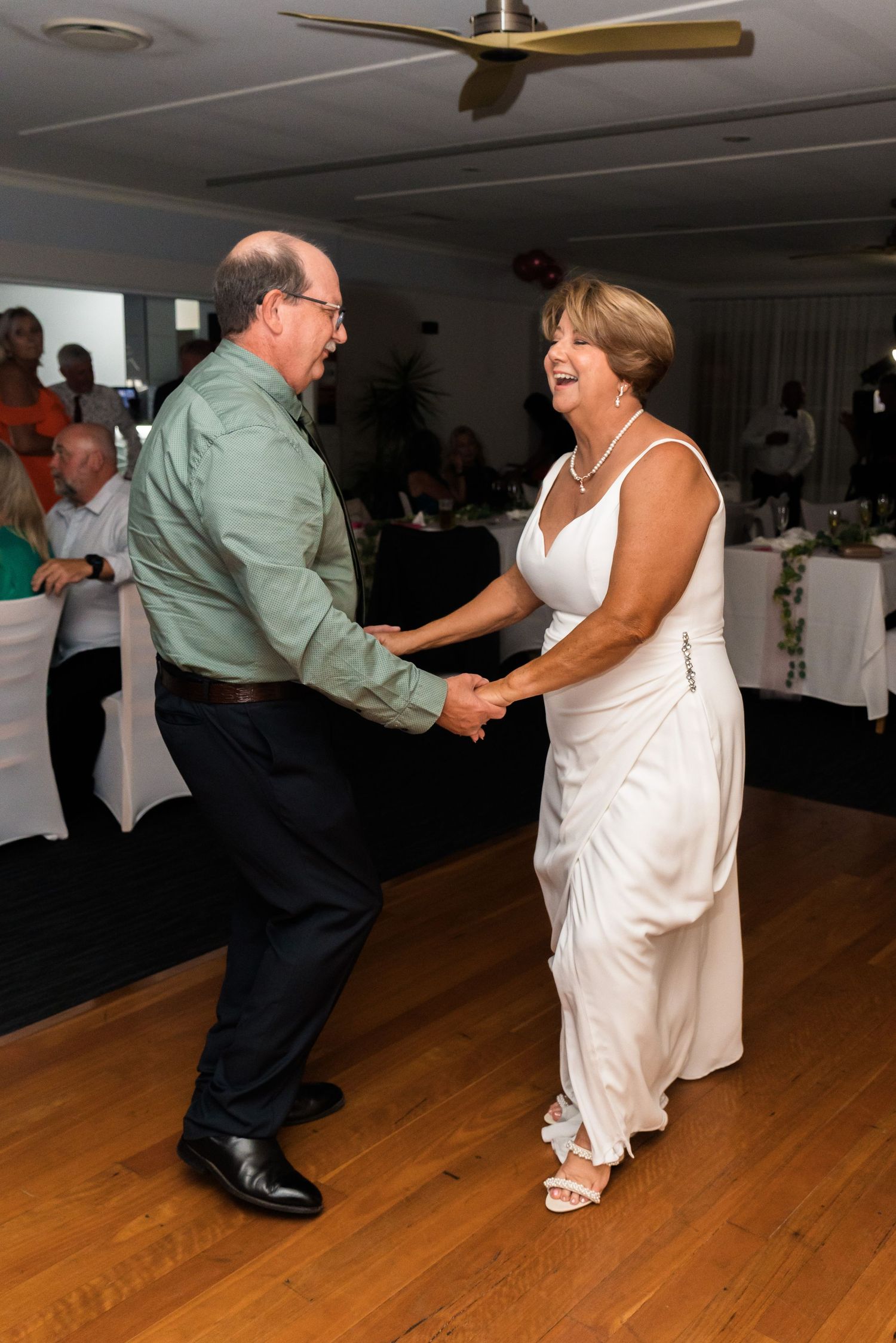 Couple dancing and laughing together on a wooden dance floor at a wedding reception.