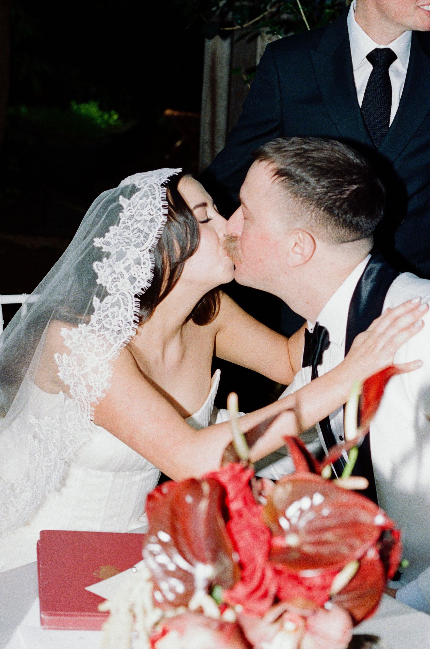 A romantic moment at a wedding reception with red floral decorations on the table.