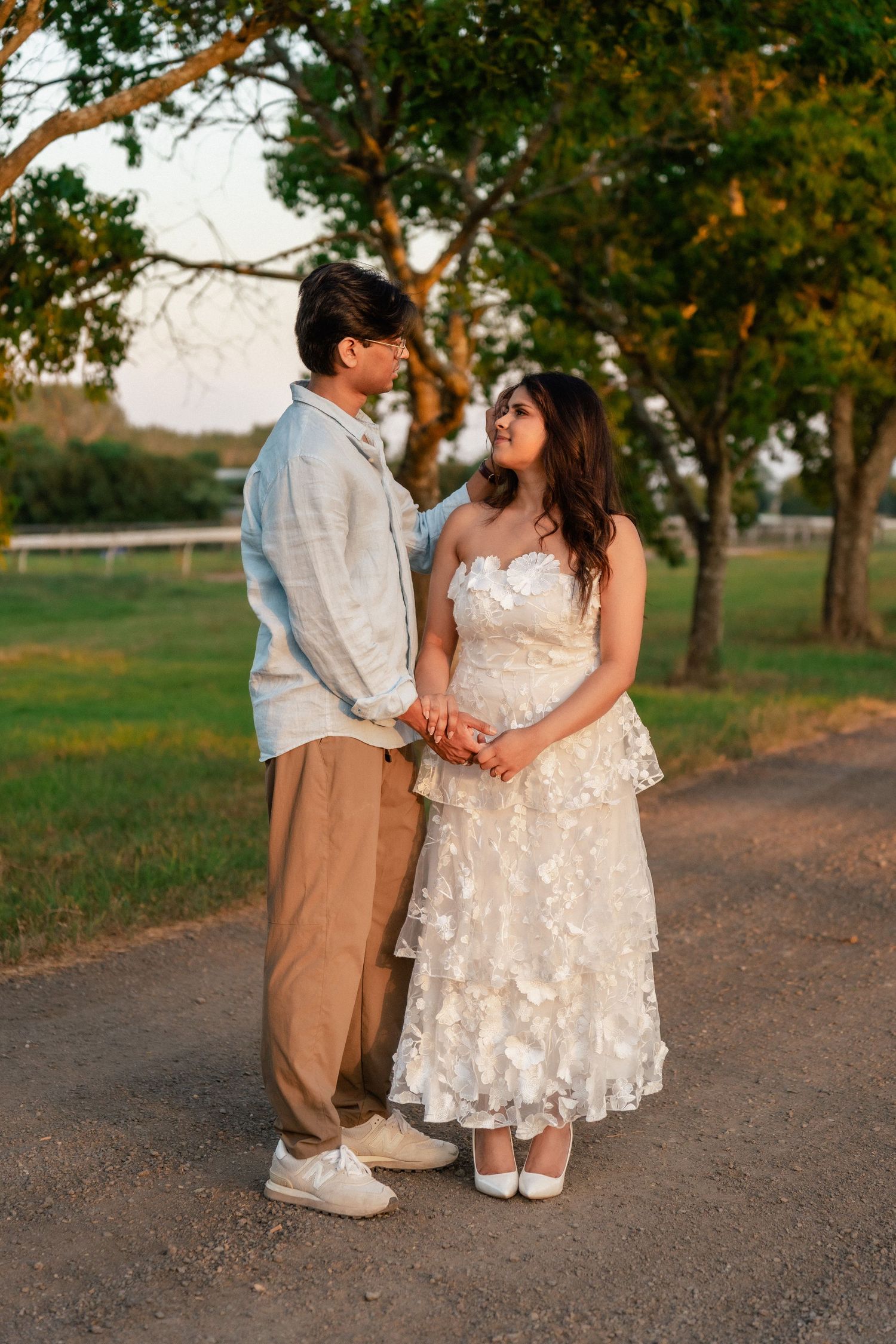 A couple in formal attire shares sweet moments on a tree-lined path at sunset.