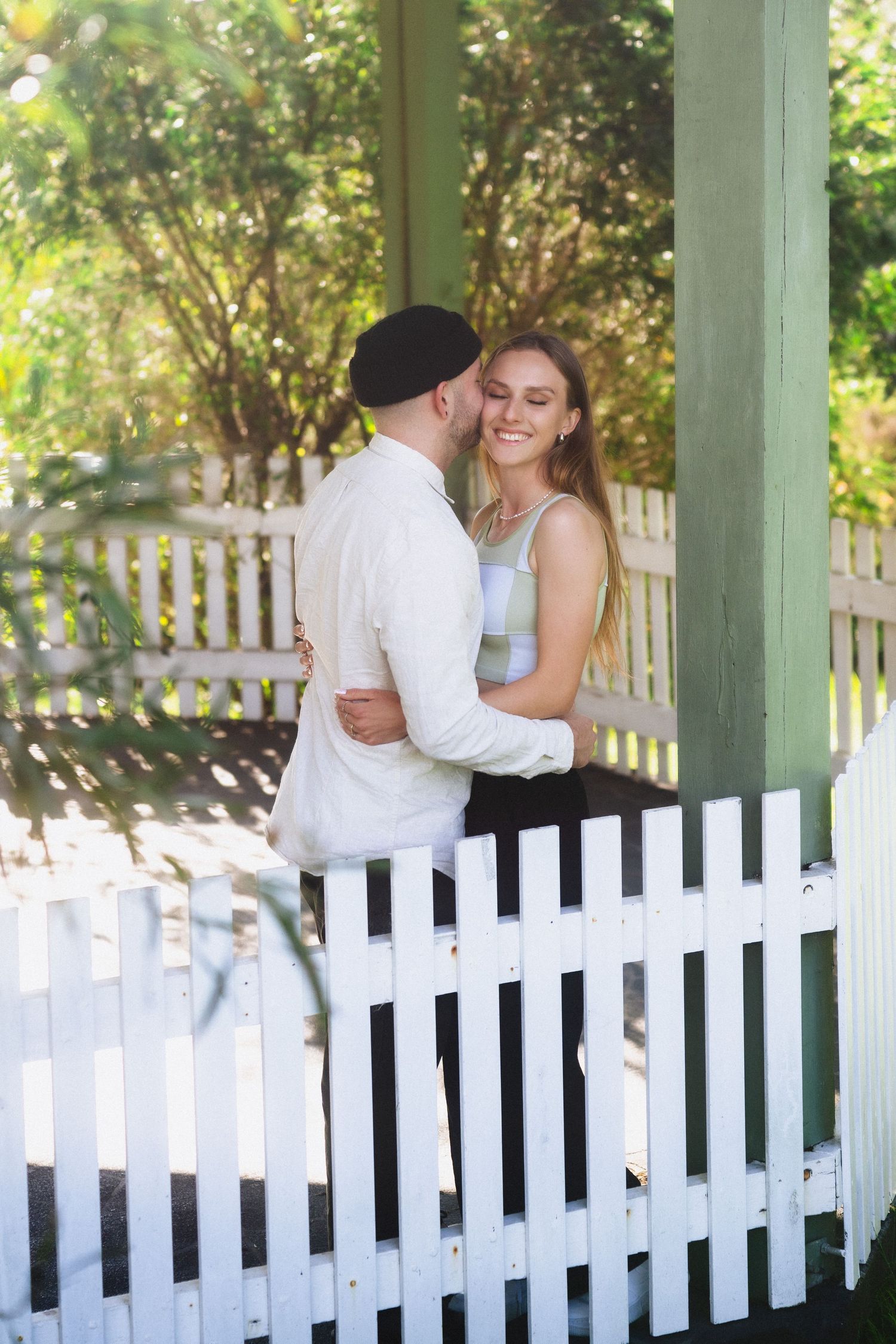 Couple sharing romantic moment by white picket fence in garden setting.