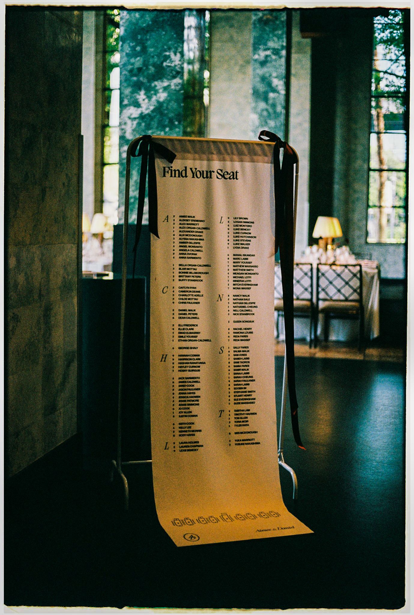 Elegant wedding seating chart scroll displayed on a stand with 'Find Your Seat' header in a dimly lit venue.