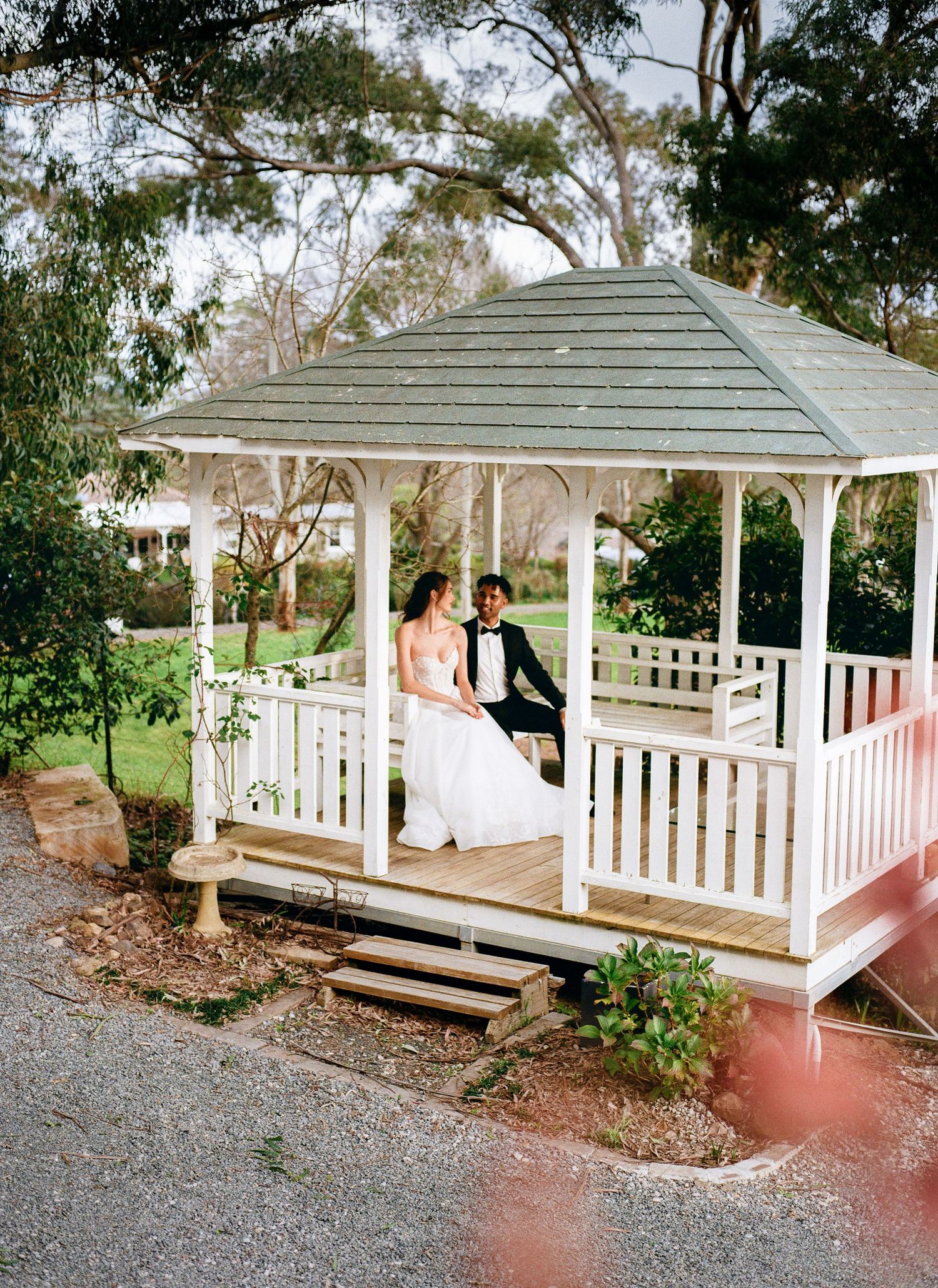 A romantic moment in a white wooden gazebo surrounded by lush greenery.
