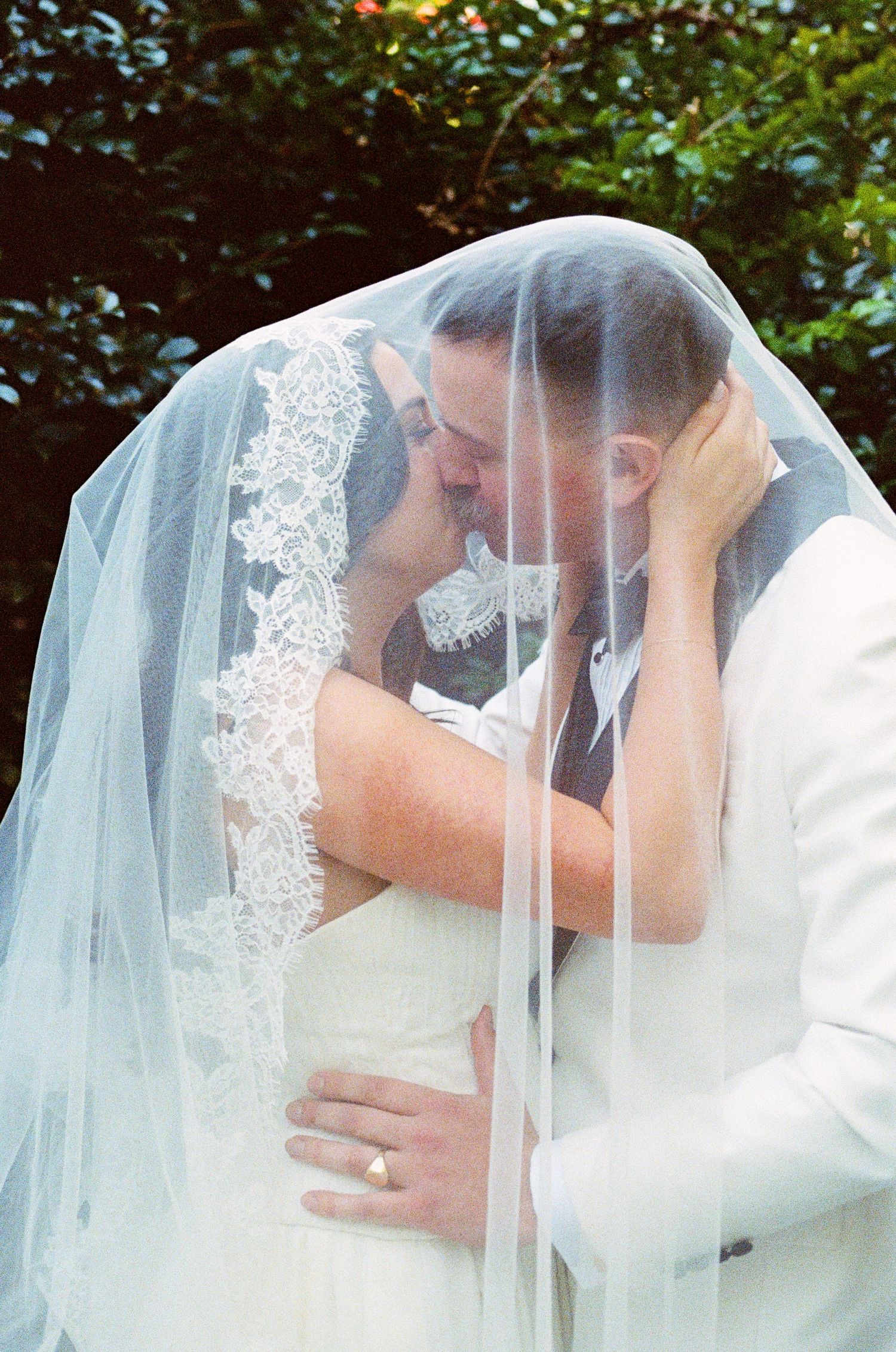 Romantic wedding kiss sequence through a delicate lace veil in an outdoor garden setting.