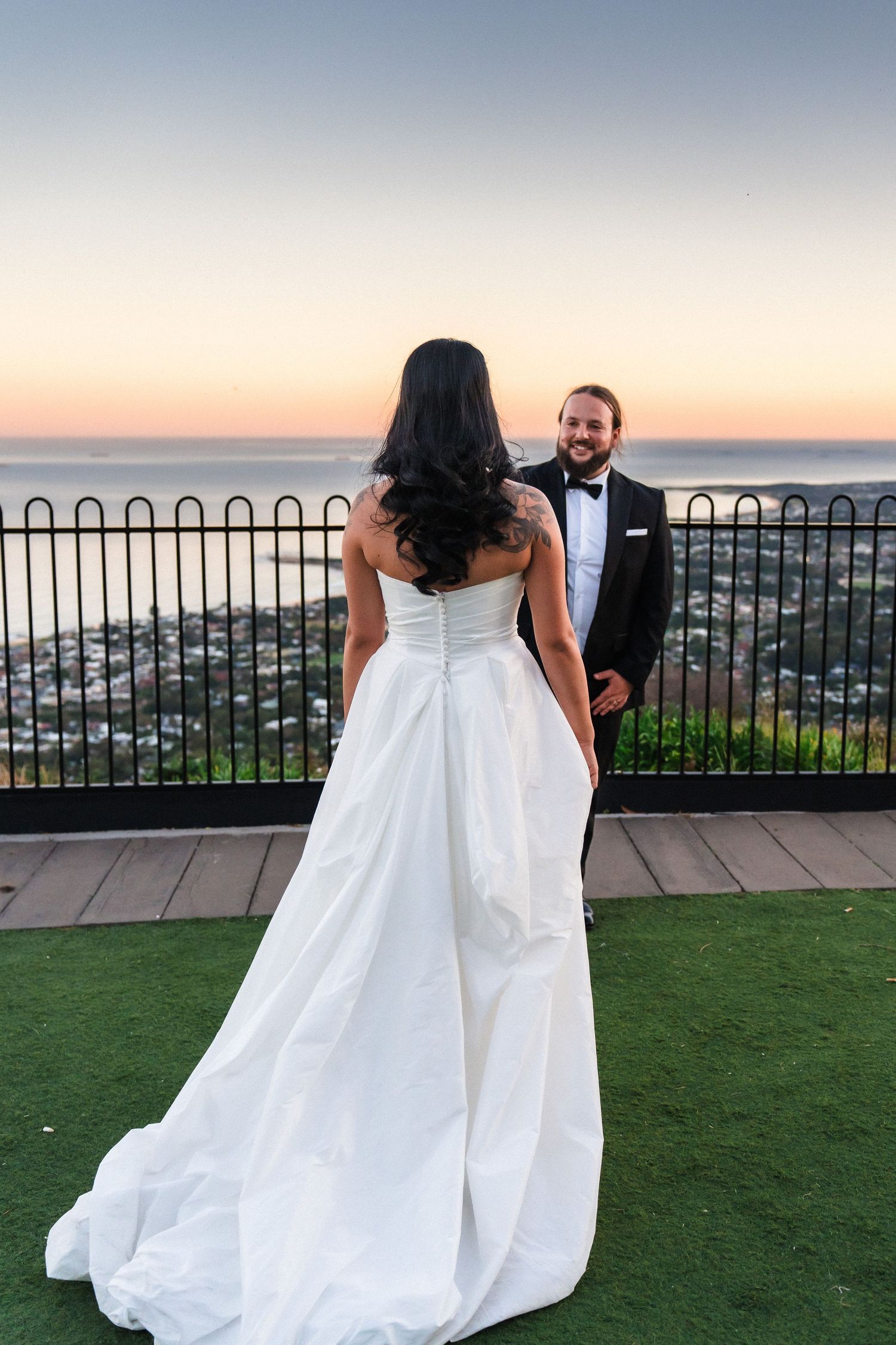 Couple in wedding attire walking along scenic overlook at sunset.