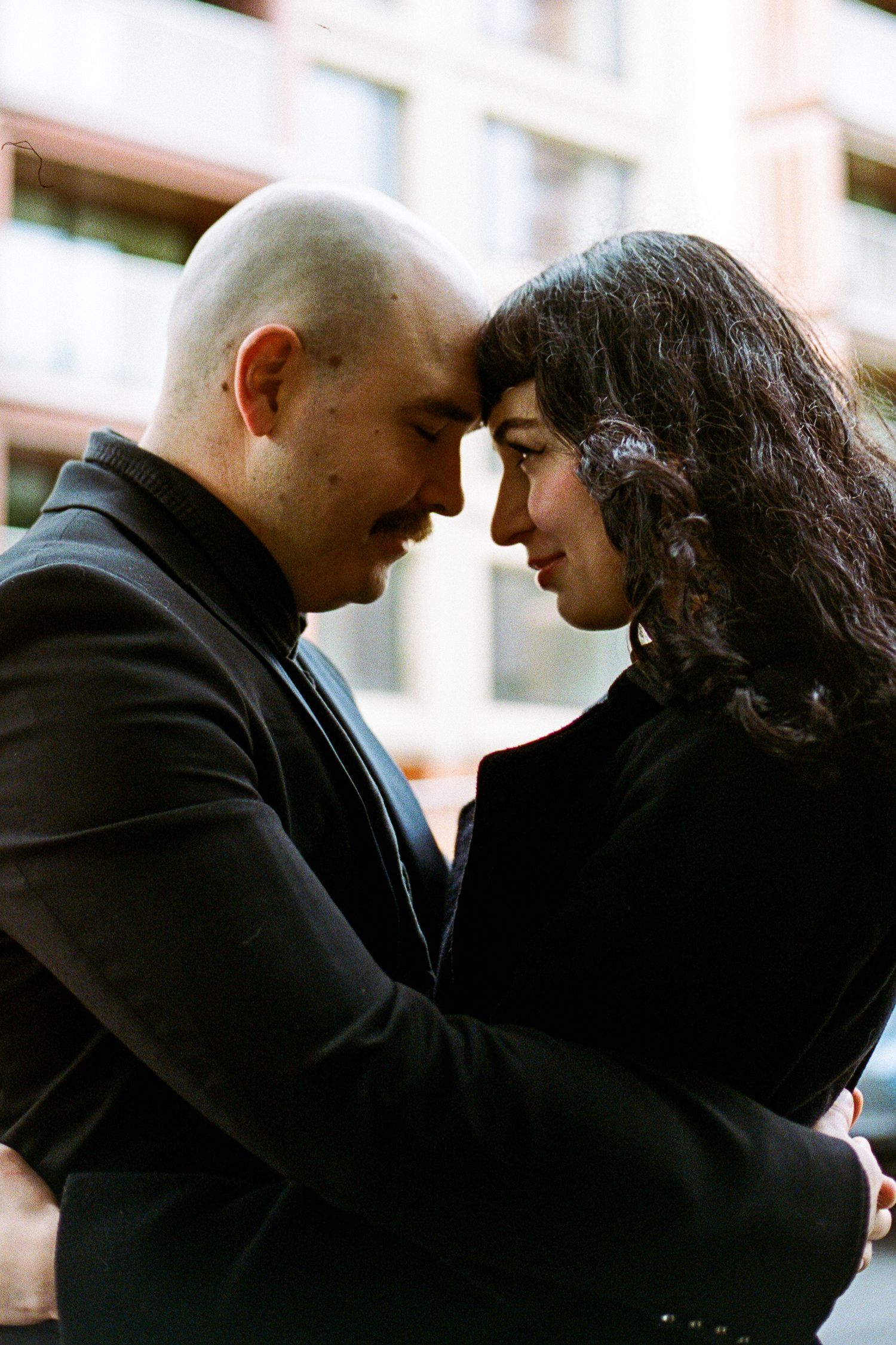 A tender moment captured between two people in black clothing against an urban backdrop.
