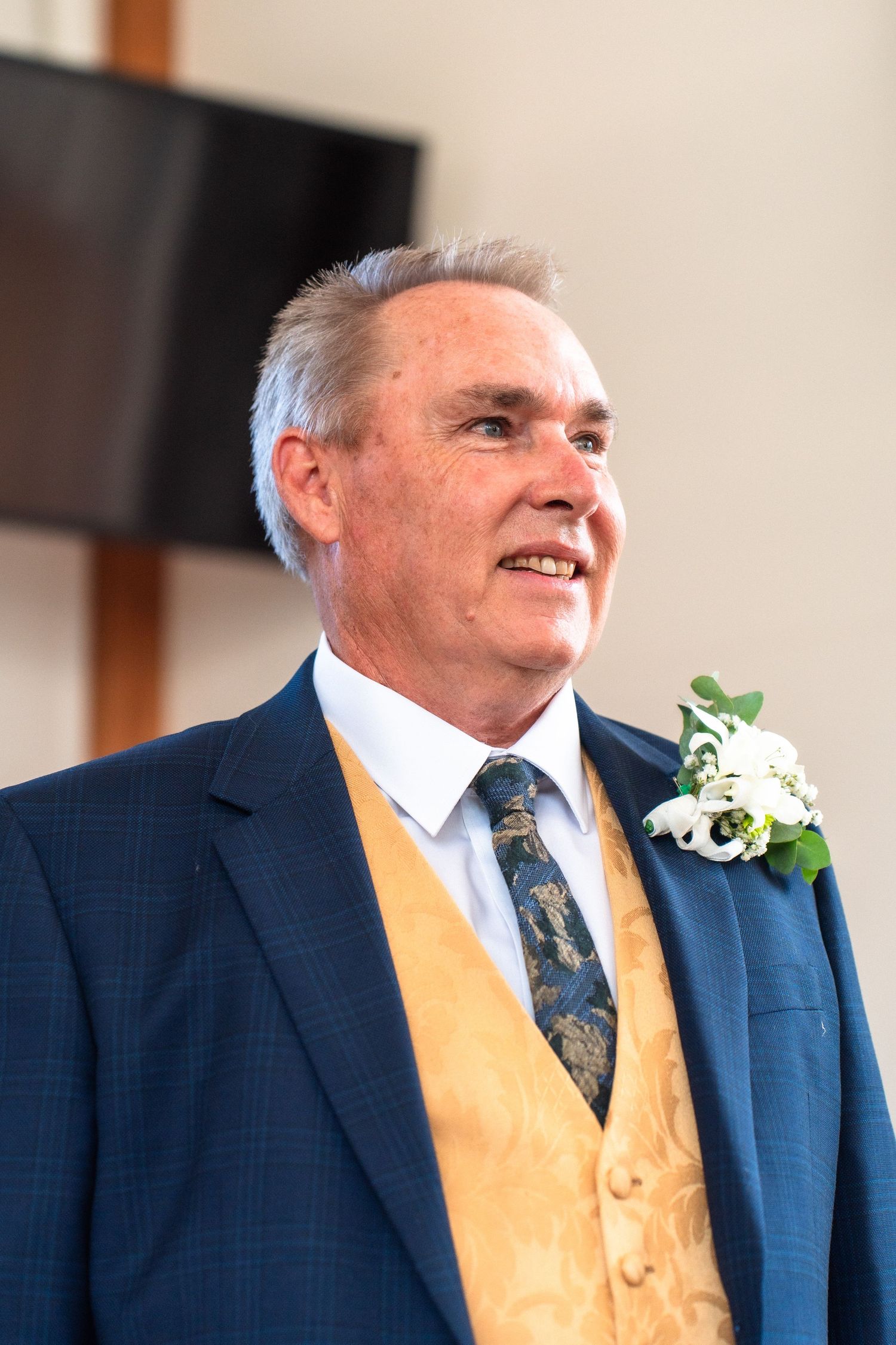 Person wearing navy suit with yellow vest and floral boutonniere.