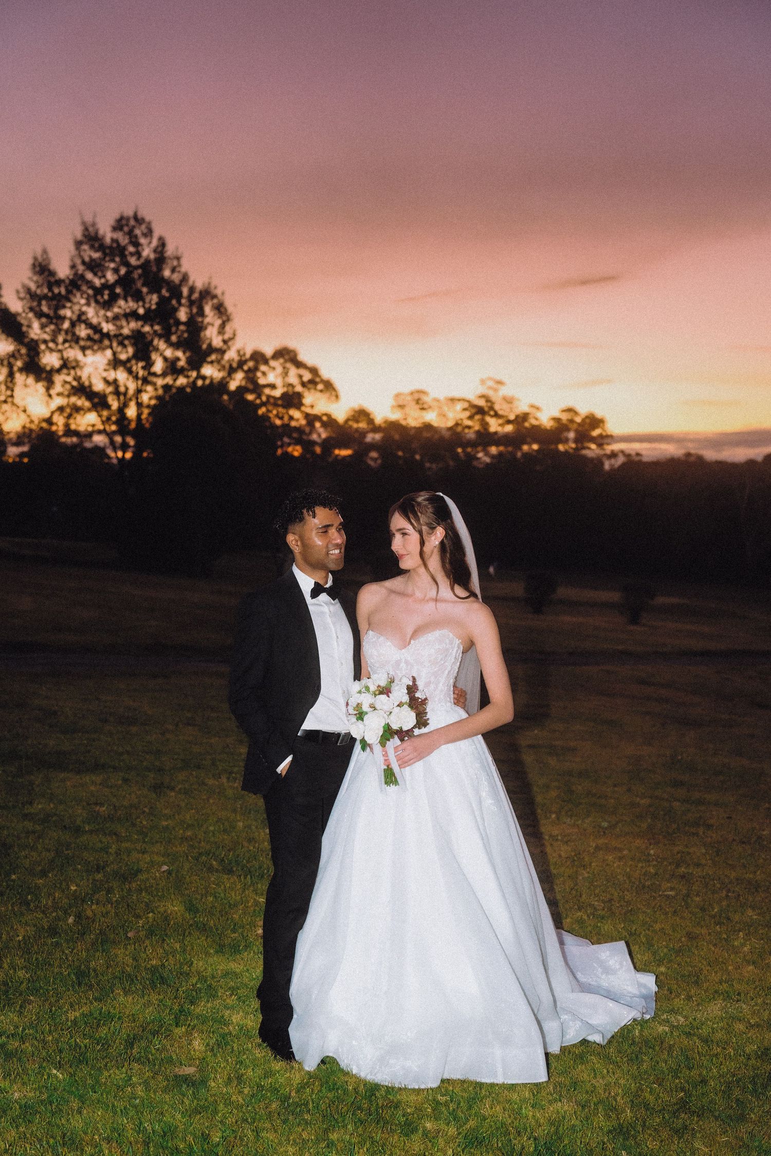 Romantic sunset wedding portrait in field with dramatic pink and purple sky.