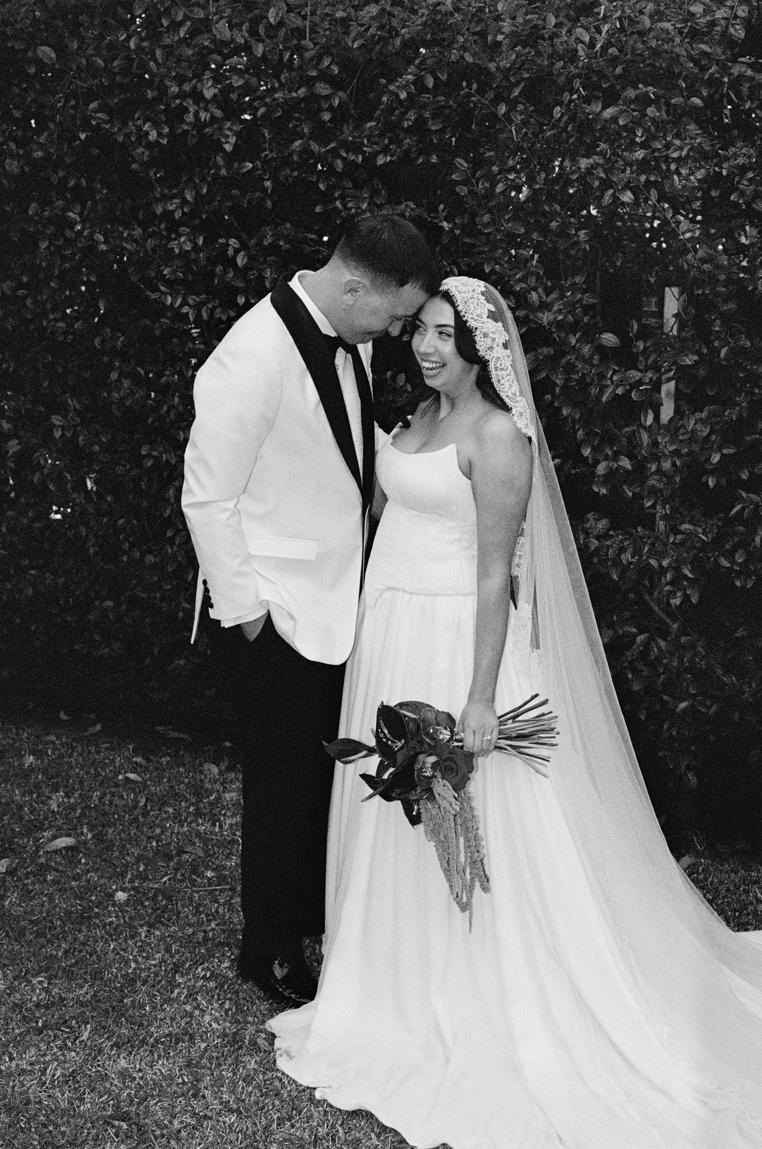 Black and white wedding portrait in a garden with elegant formal attire.