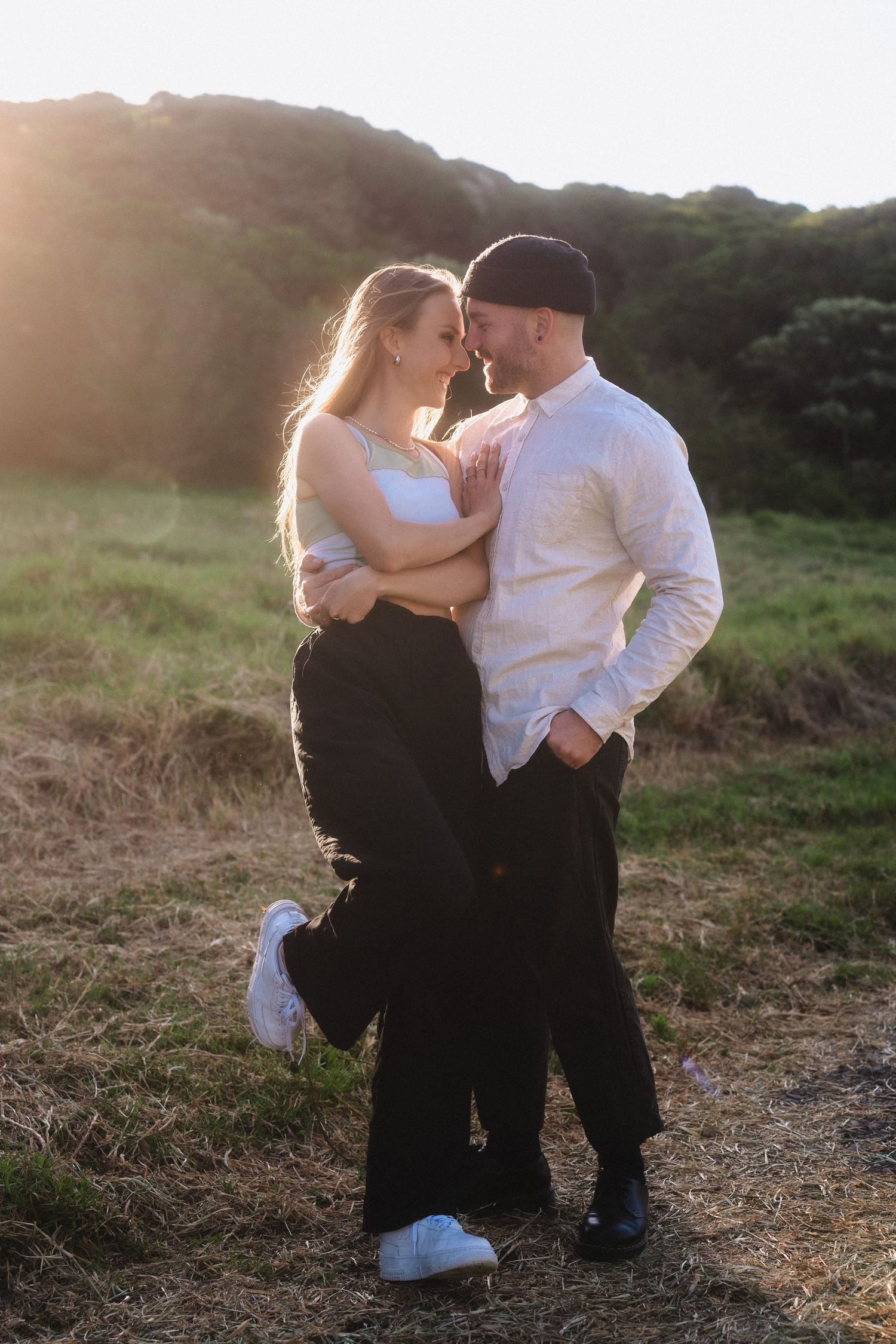 Romantic sunset photos of a couple sharing intimate moments in a grassy field.