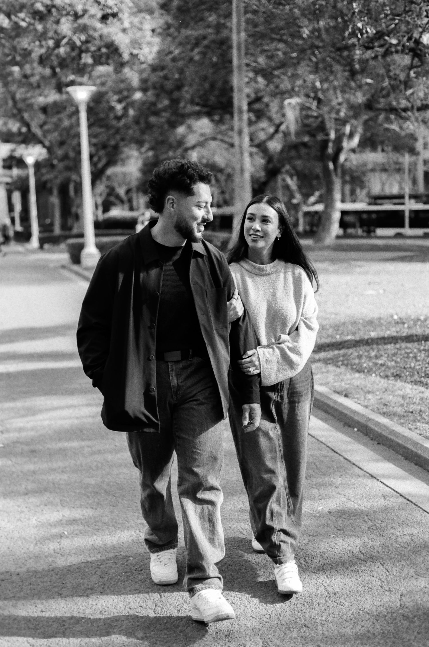 A couple walks together laughing on a park pathway.