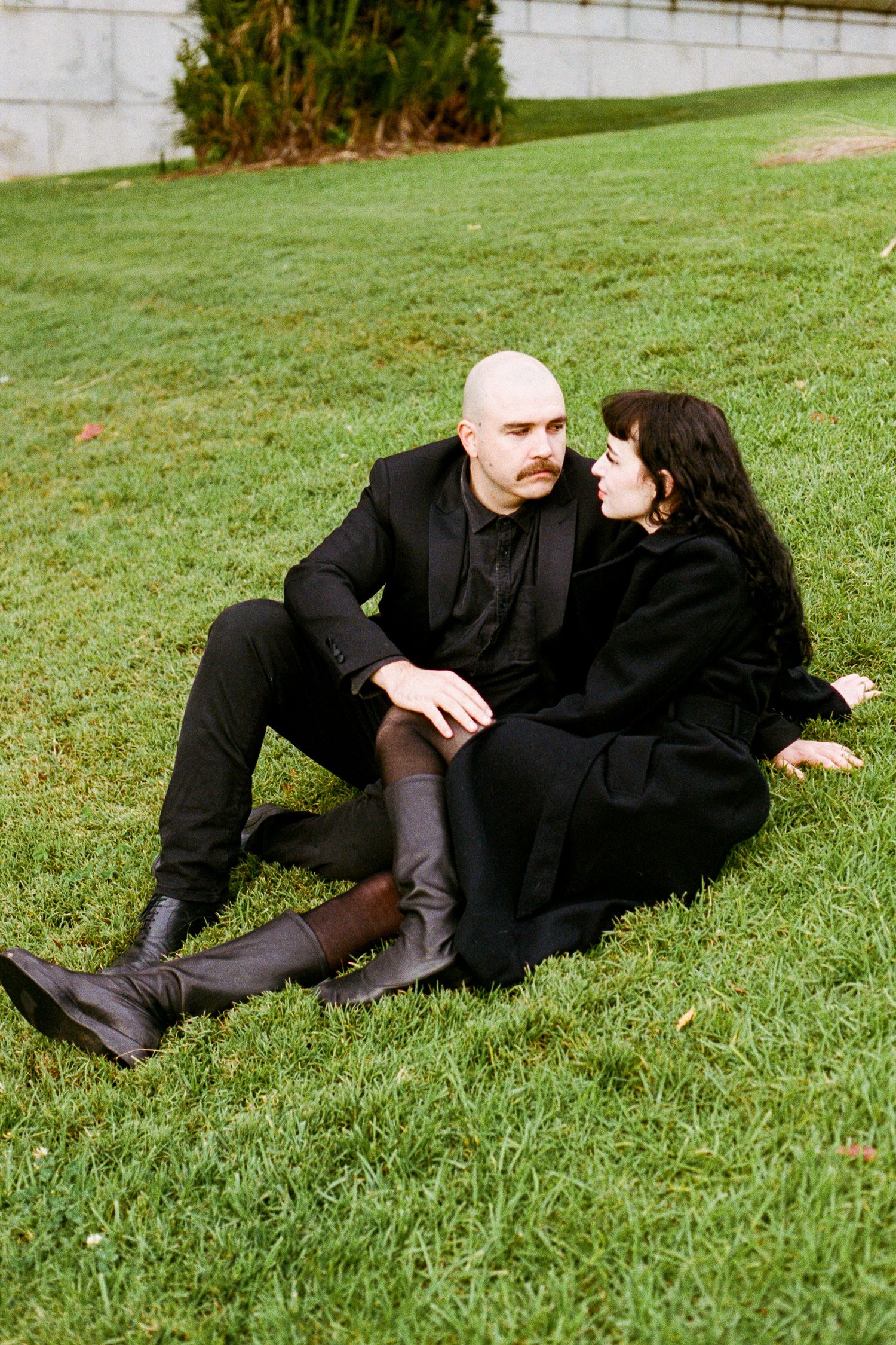 Couple lying together on green grass wearing matching black outfits.