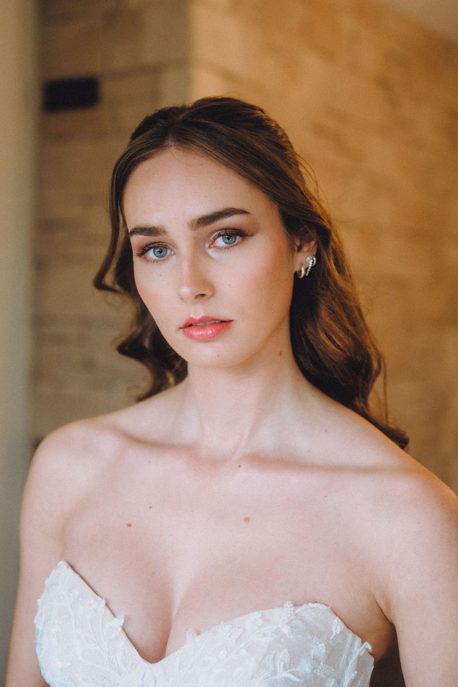 Close-up bridal portrait showcasing intricate lace bodice and romantic makeup against warm backdrop.