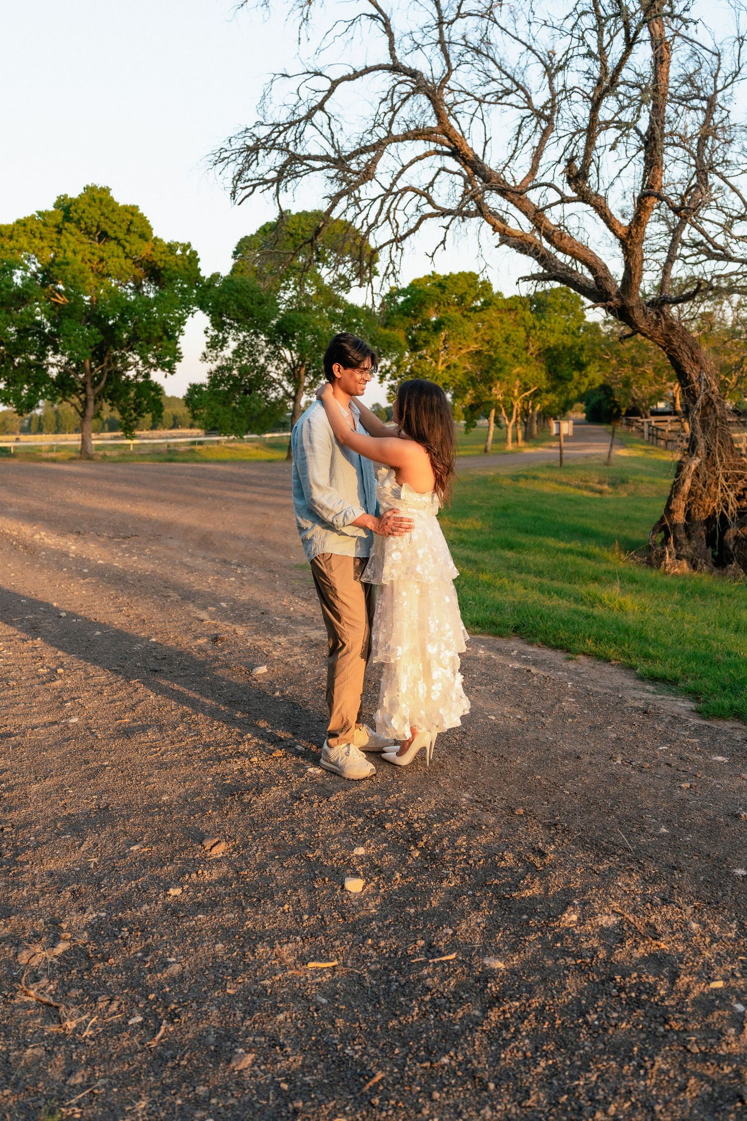 A couple poses together in a grassy field during golden hour with trees in the background.