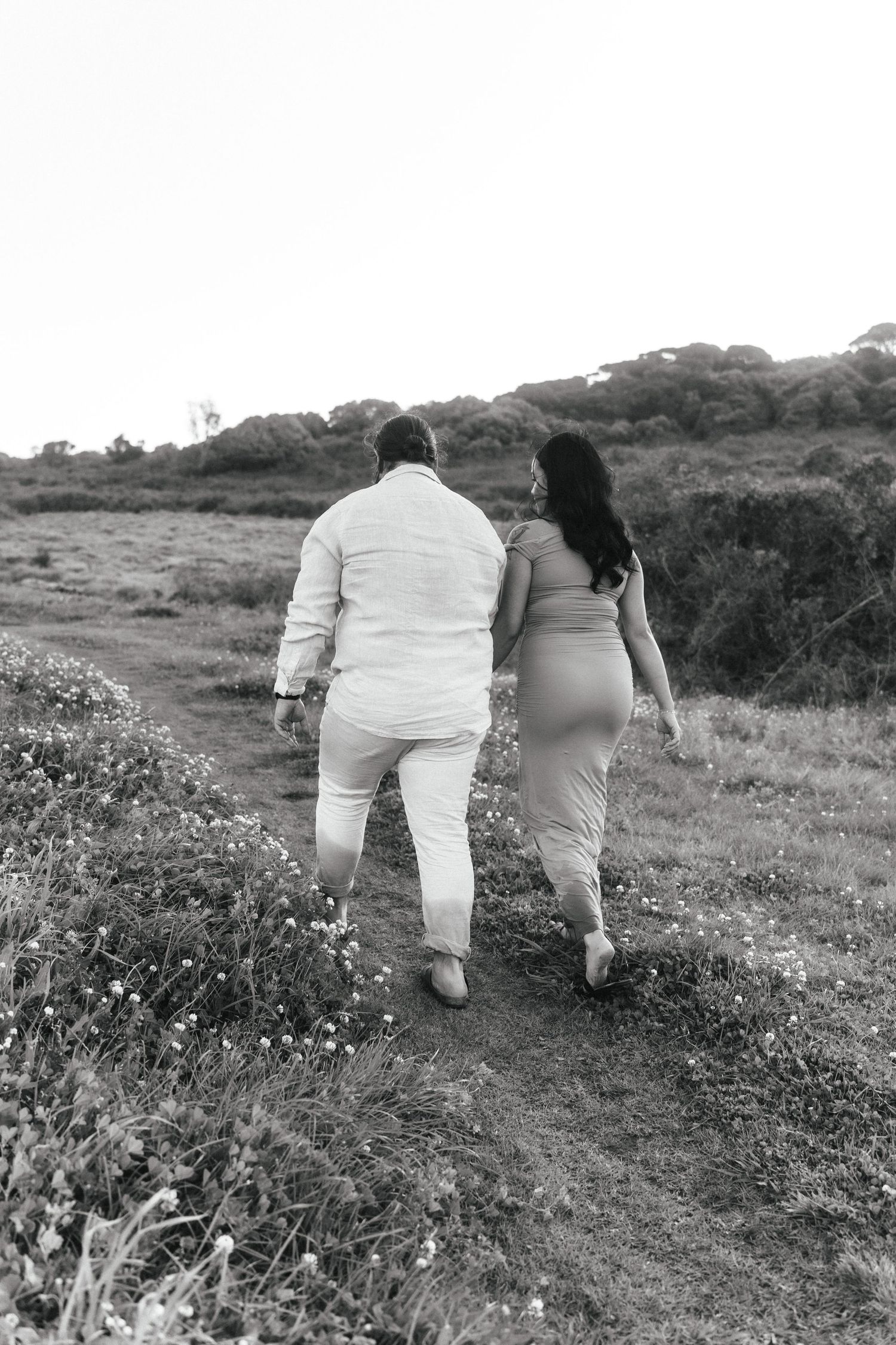 A couple walks together on a hillside path surrounded by wildflowers.