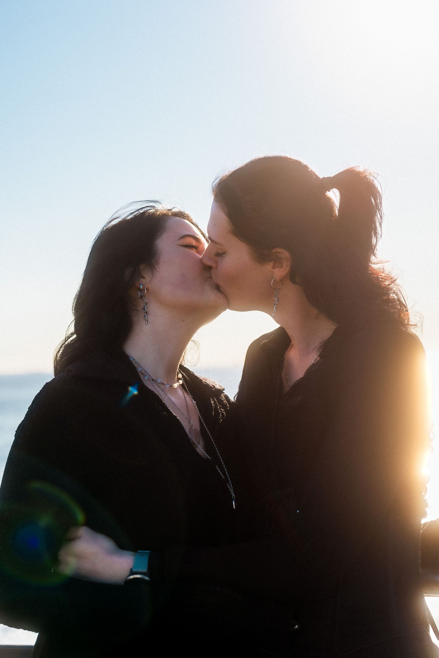 A couple shares a silhouetted kiss against a bright sunlit sky.