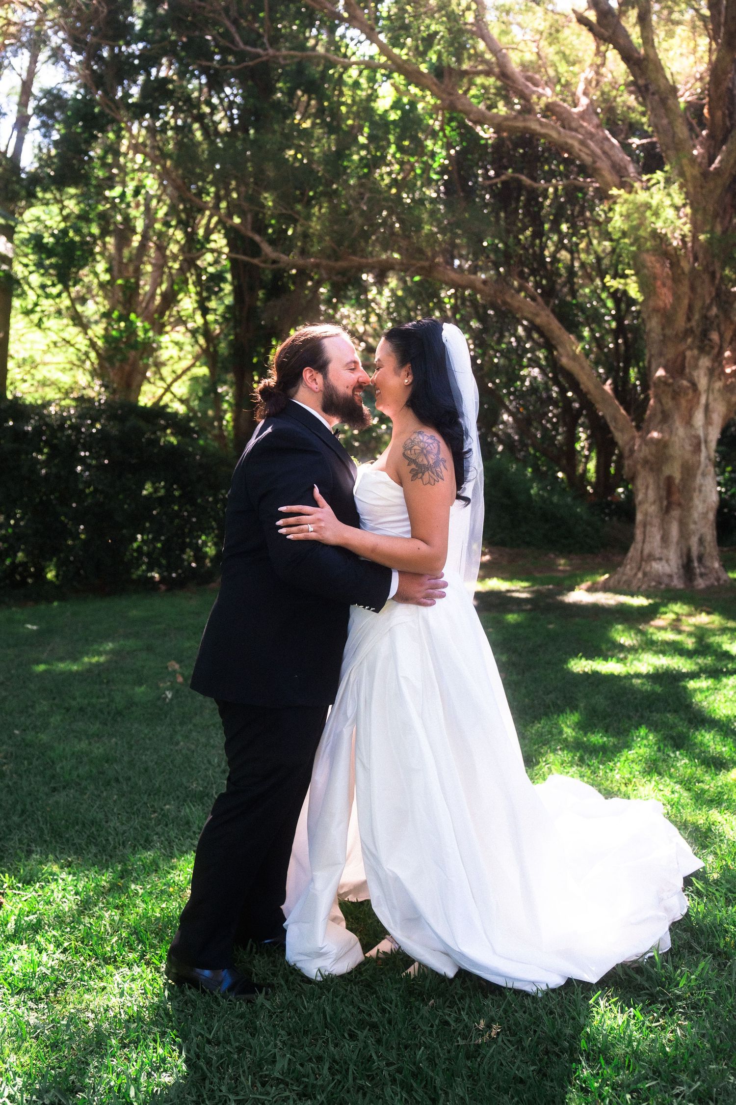 Wedding couple shares intimate moments on grass under sunlit trees.
