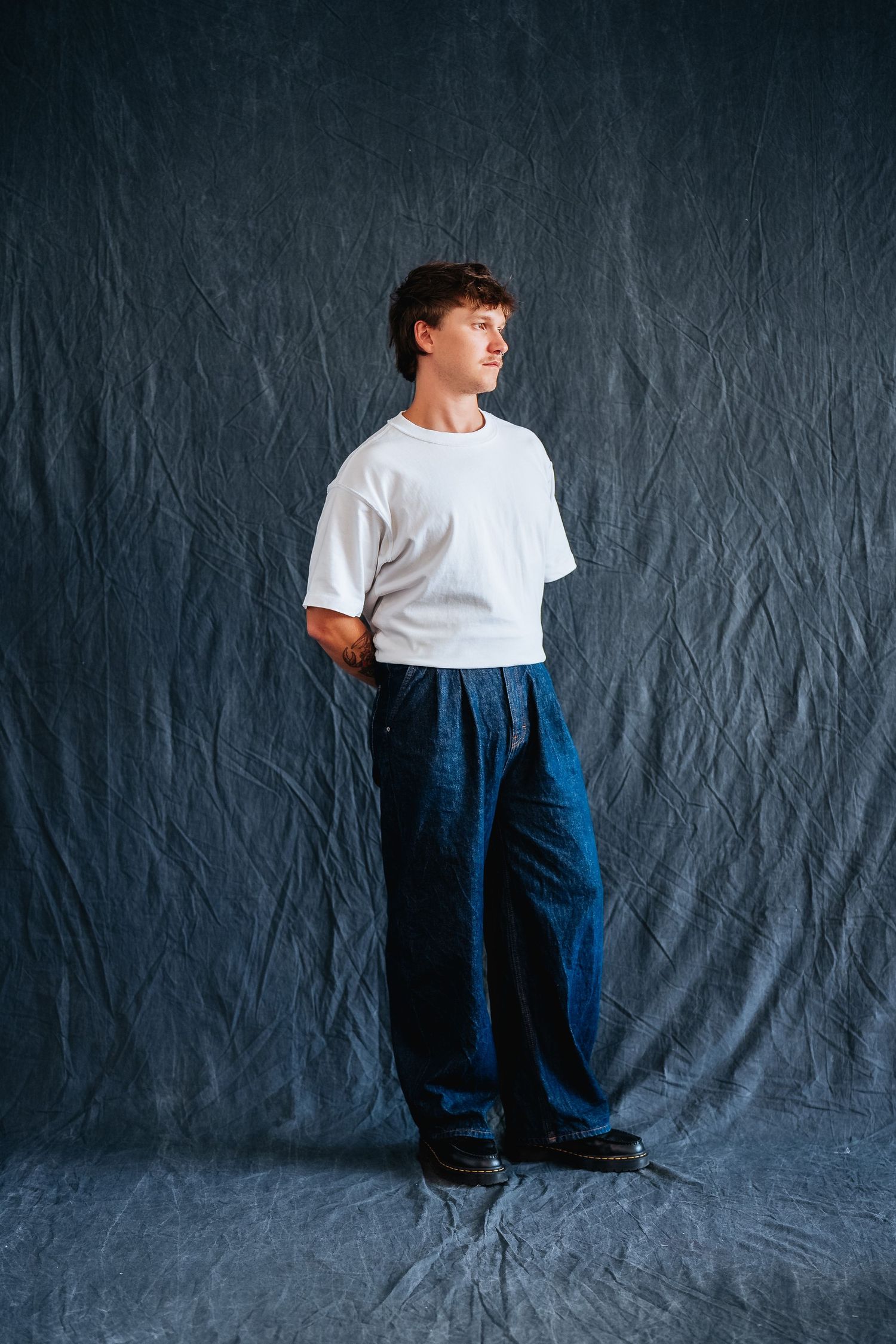Stylish casual pose against textured navy backdrop in white tee and wide-leg pants.
