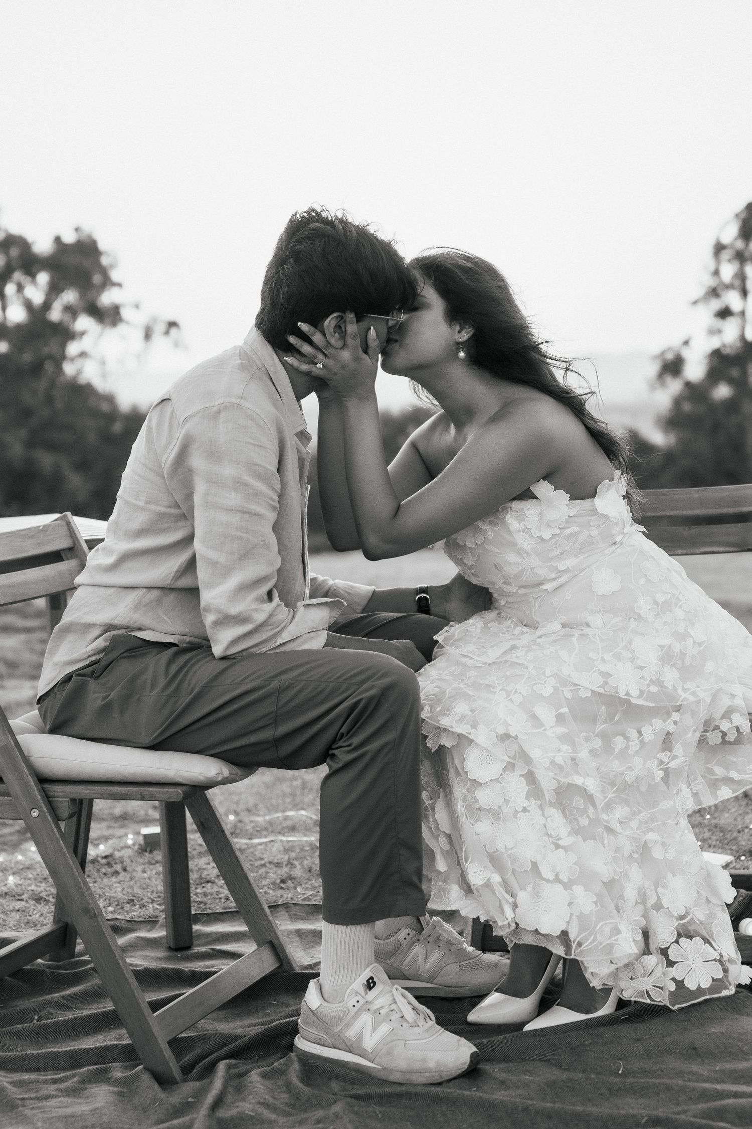 Intimate black and white photo of a couple sharing a tender moment on a wooden bench.