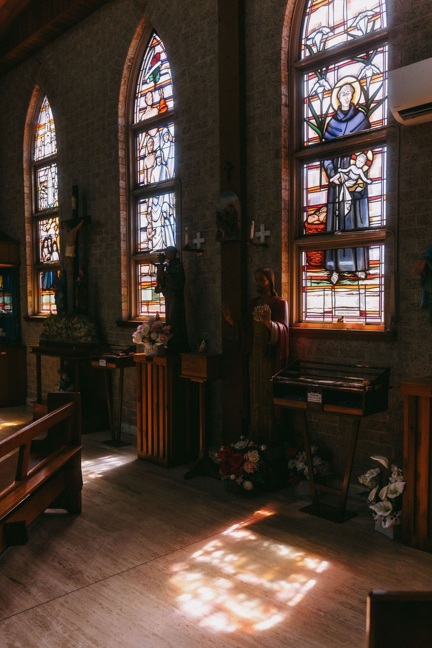 Warm sunlight casts geometric patterns through stained glass windows in a church interior.