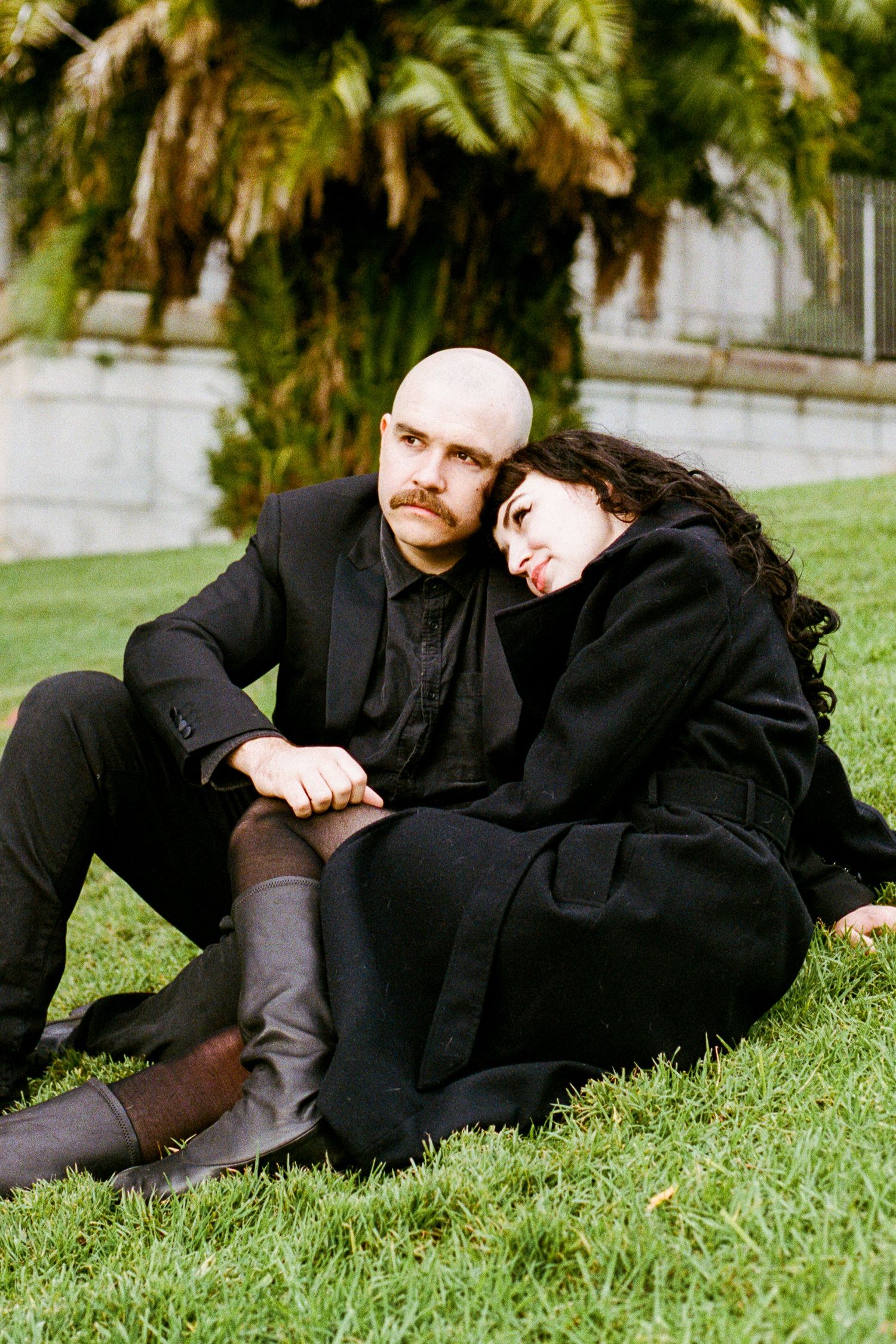 A couple in black clothing relaxes together on green grass.