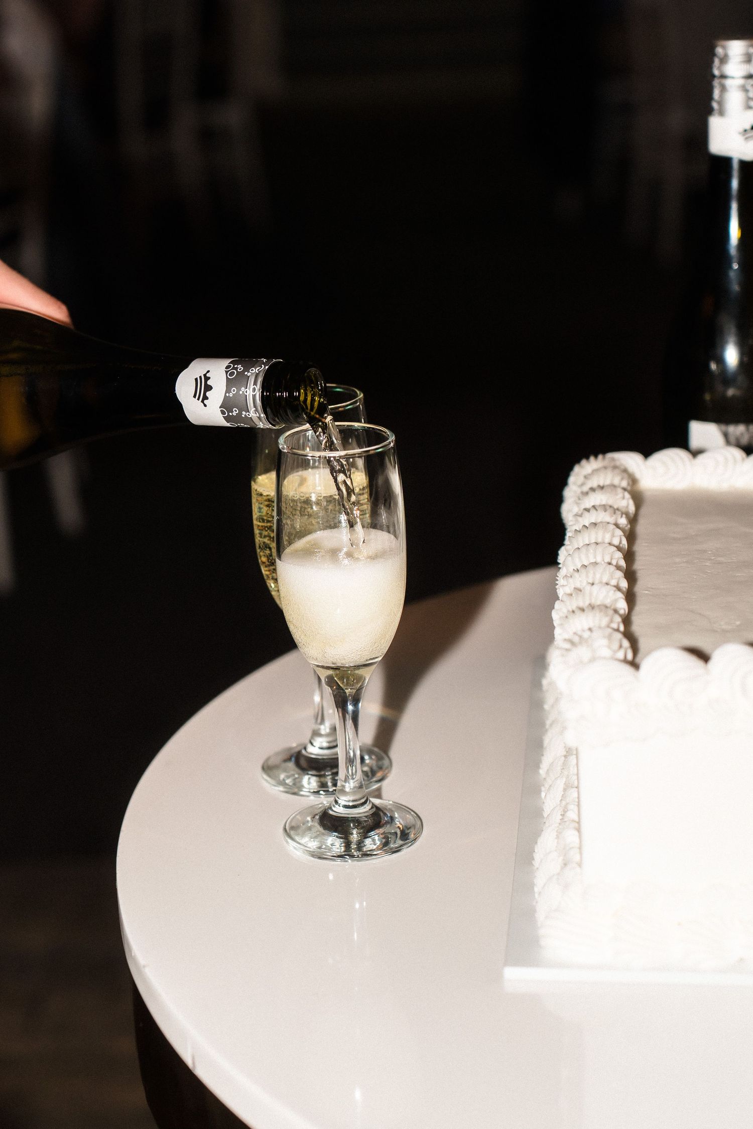 Champagne being poured into a glass next to a white wedding cake.