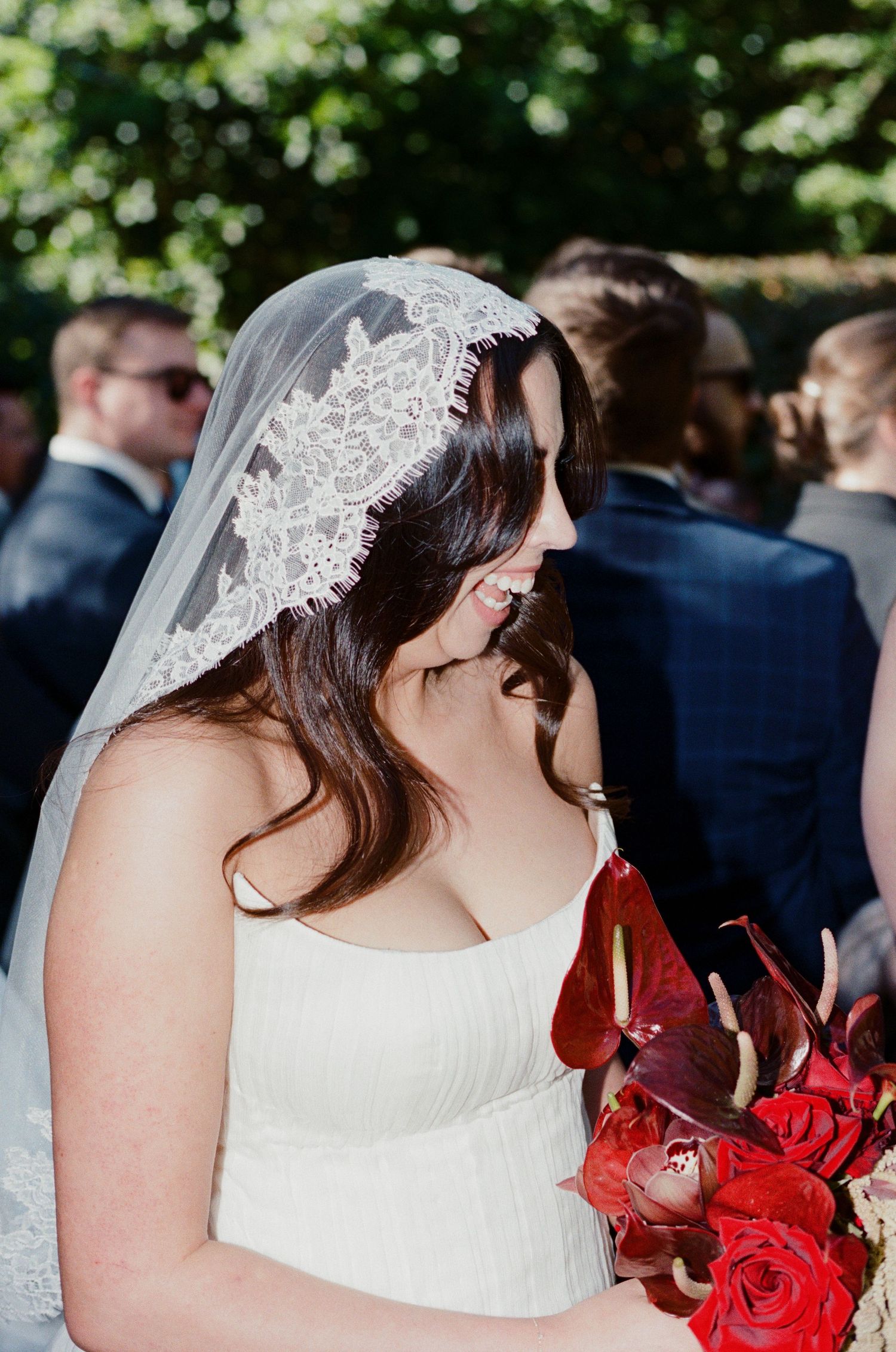 Bride holding vibrant red rose bouquet in outdoor garden setting.