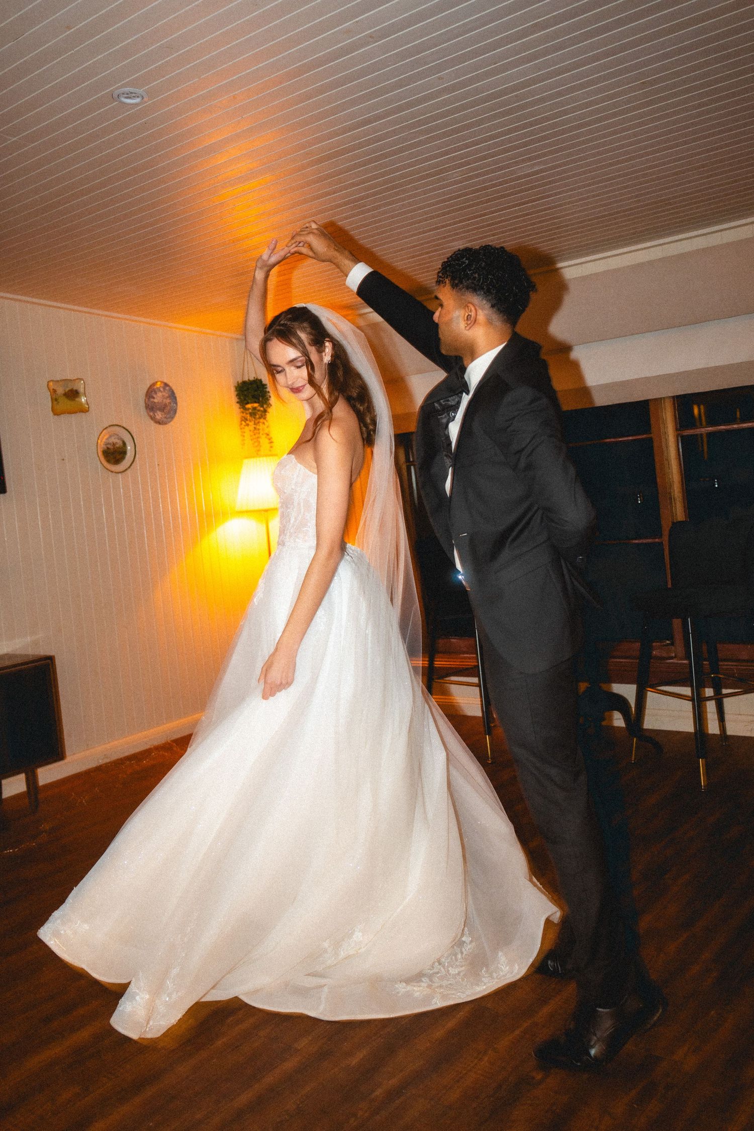 A couple dances on a wooden floor with warm lighting creating a romantic atmosphere.