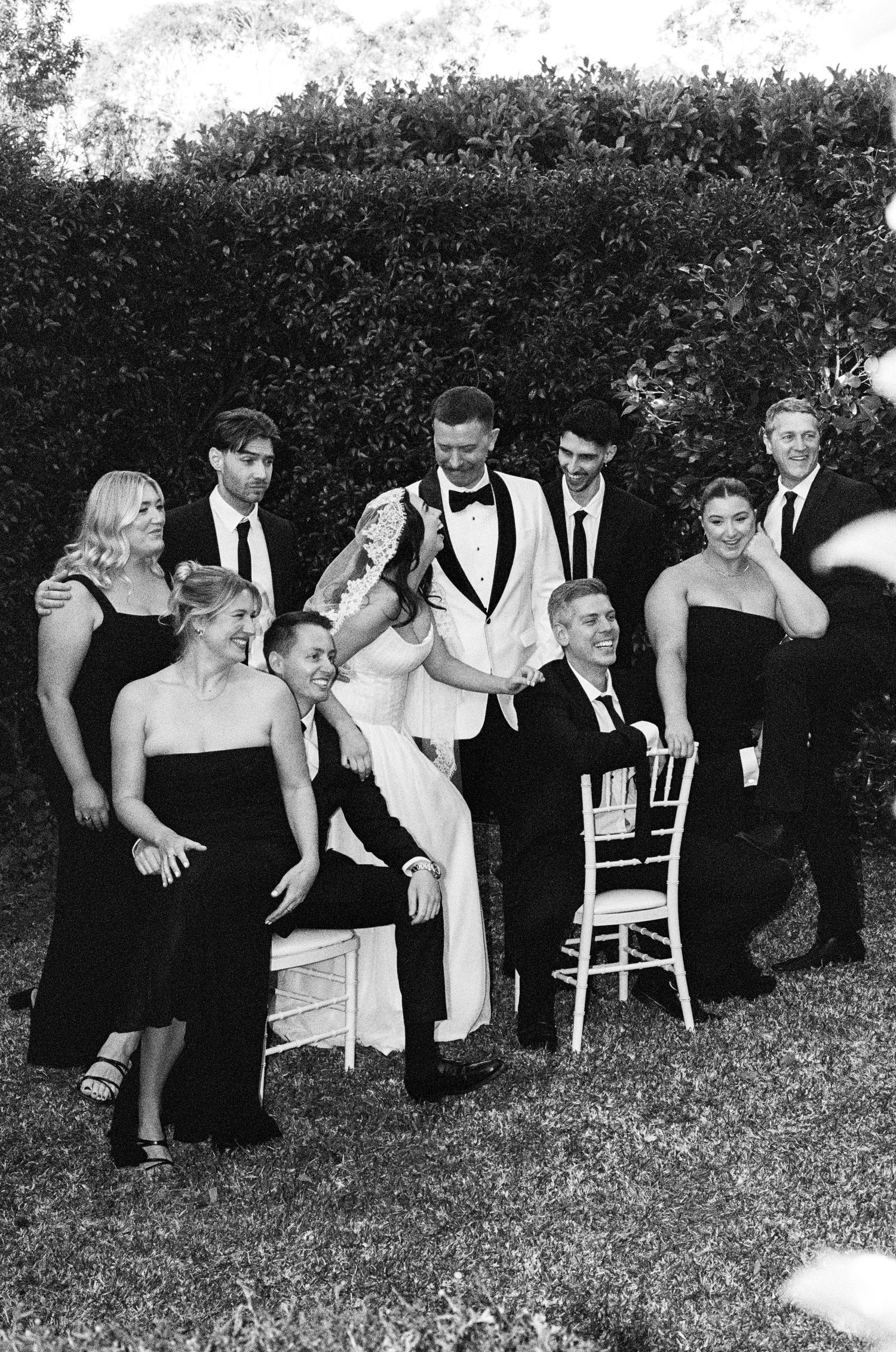Wedding party posing playfully in black and white formal attire outdoors.