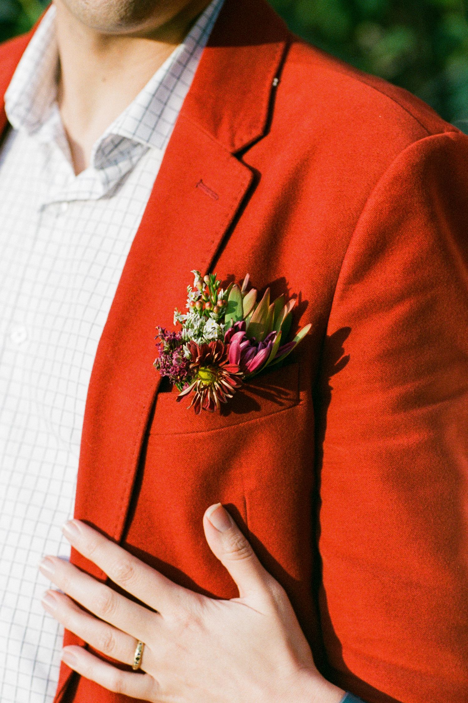 Red blazer with boutonniere and white shirt, showing wedding ring on hand.