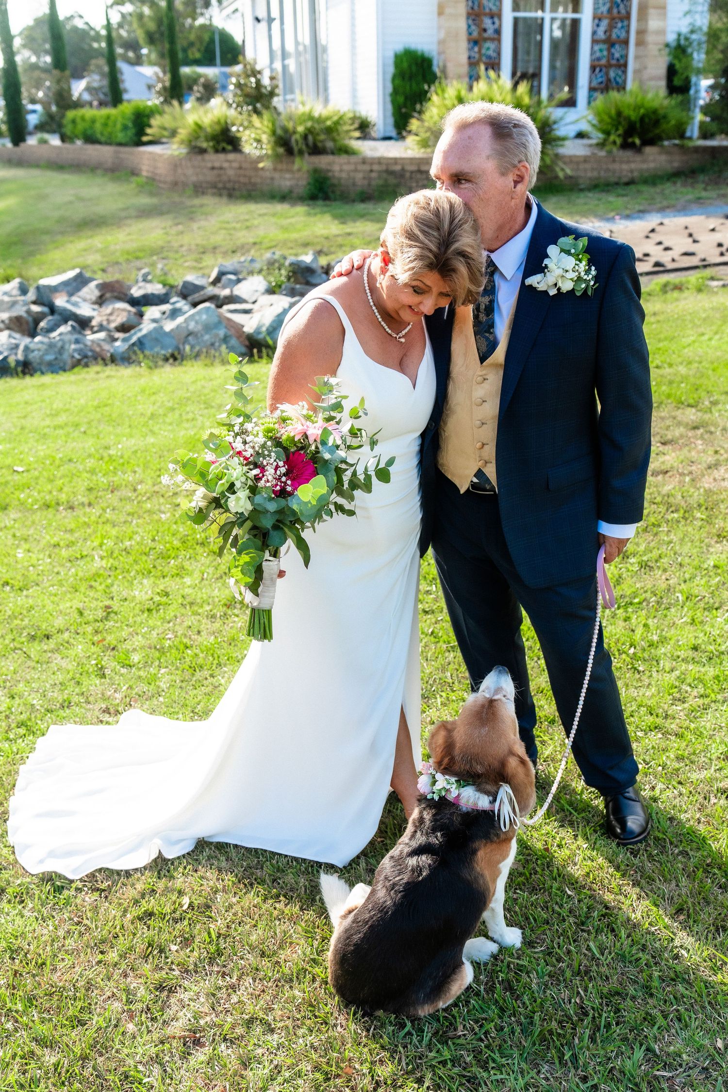 Newlyweds posing on grass with their pet dog during outdoor wedding photos.