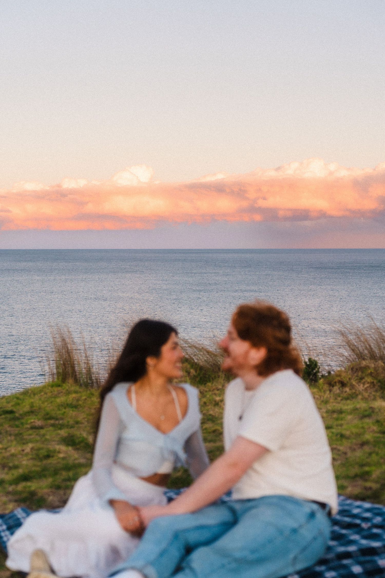 Couple sitting on picnic blanket by the ocean during a vibrant sunset.