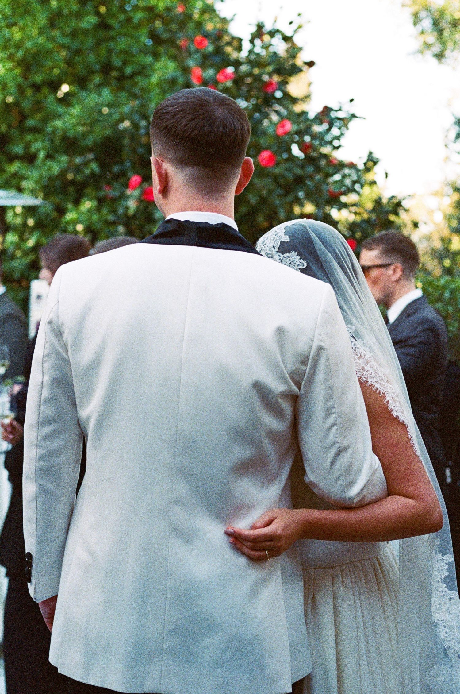 Wedding couple walking together in white formal attire against a garden backdrop.