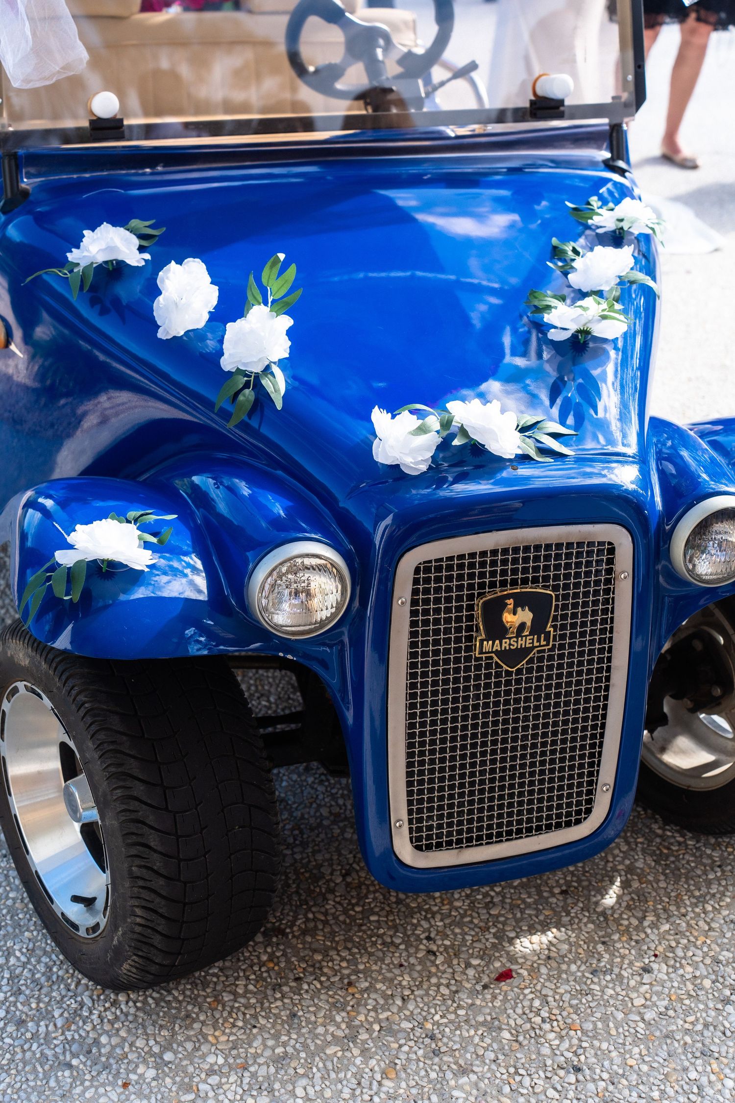 Close-up of a blue vintage car's front grille decorated with white flowers.