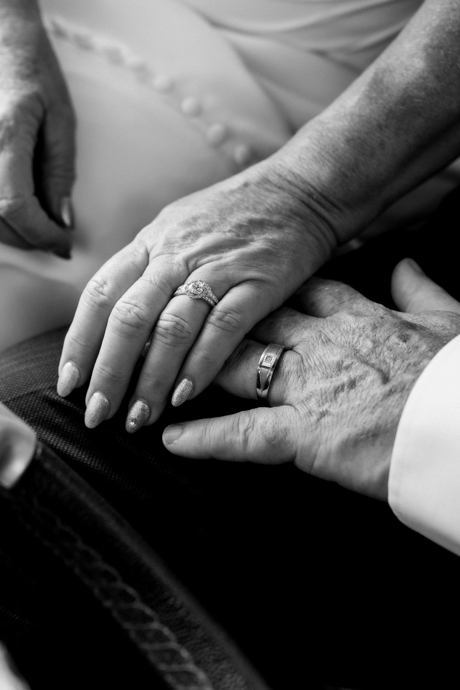 Black and white detail shots of hands with wedding rings resting on formal attire.