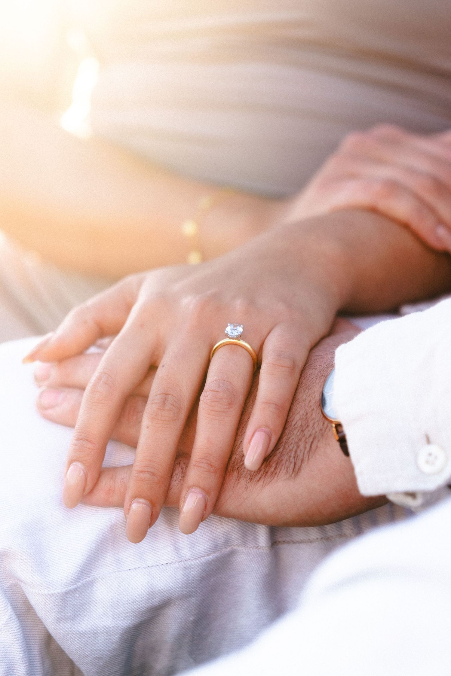 Close-up of hands with an engagement ring in warm sunlight.