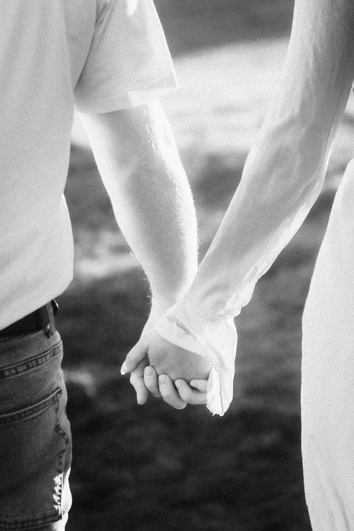A couple holds hands tenderly in a black and white close-up shot.