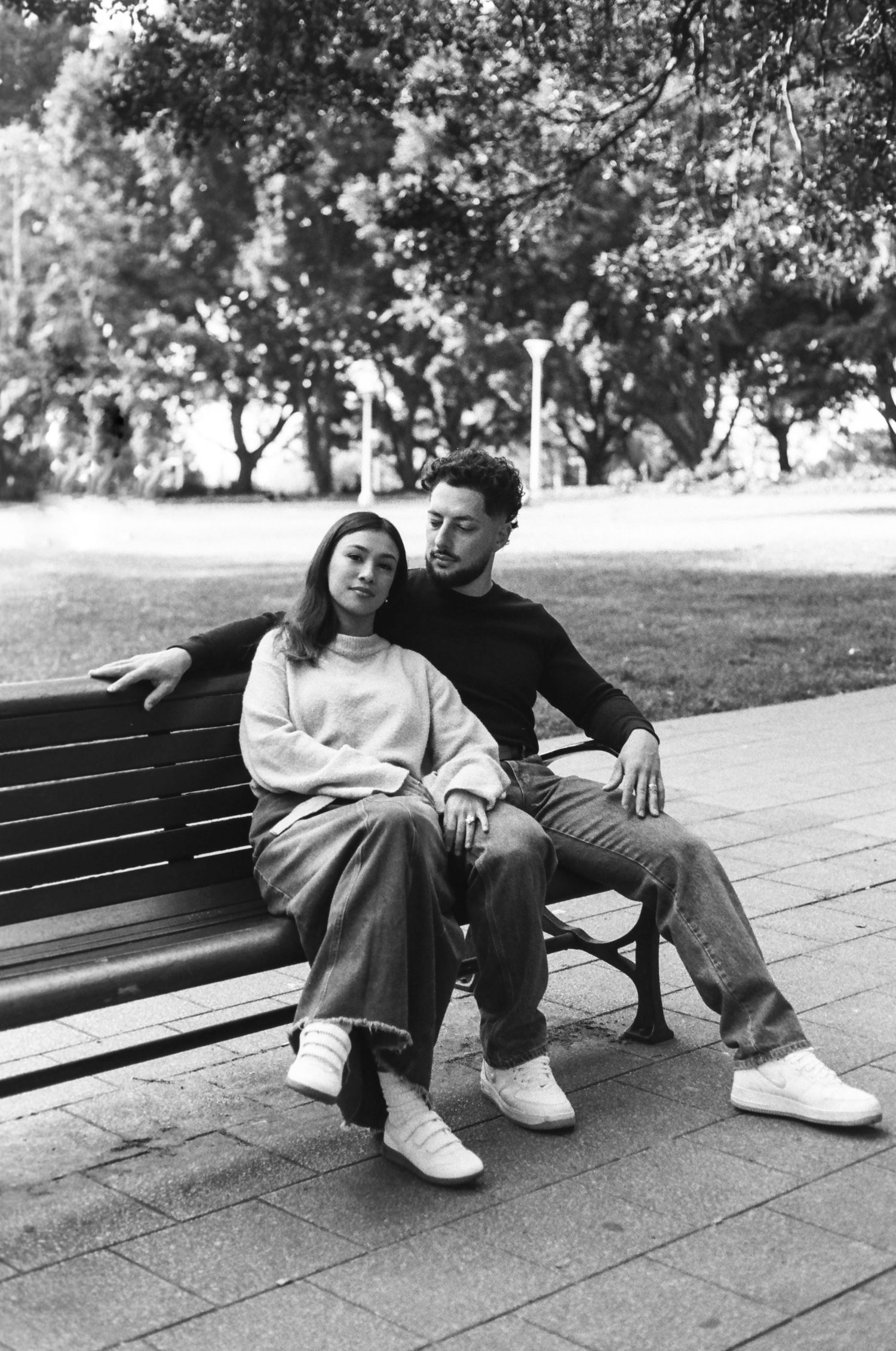A couple relaxes together on a park bench in a black and white photo.