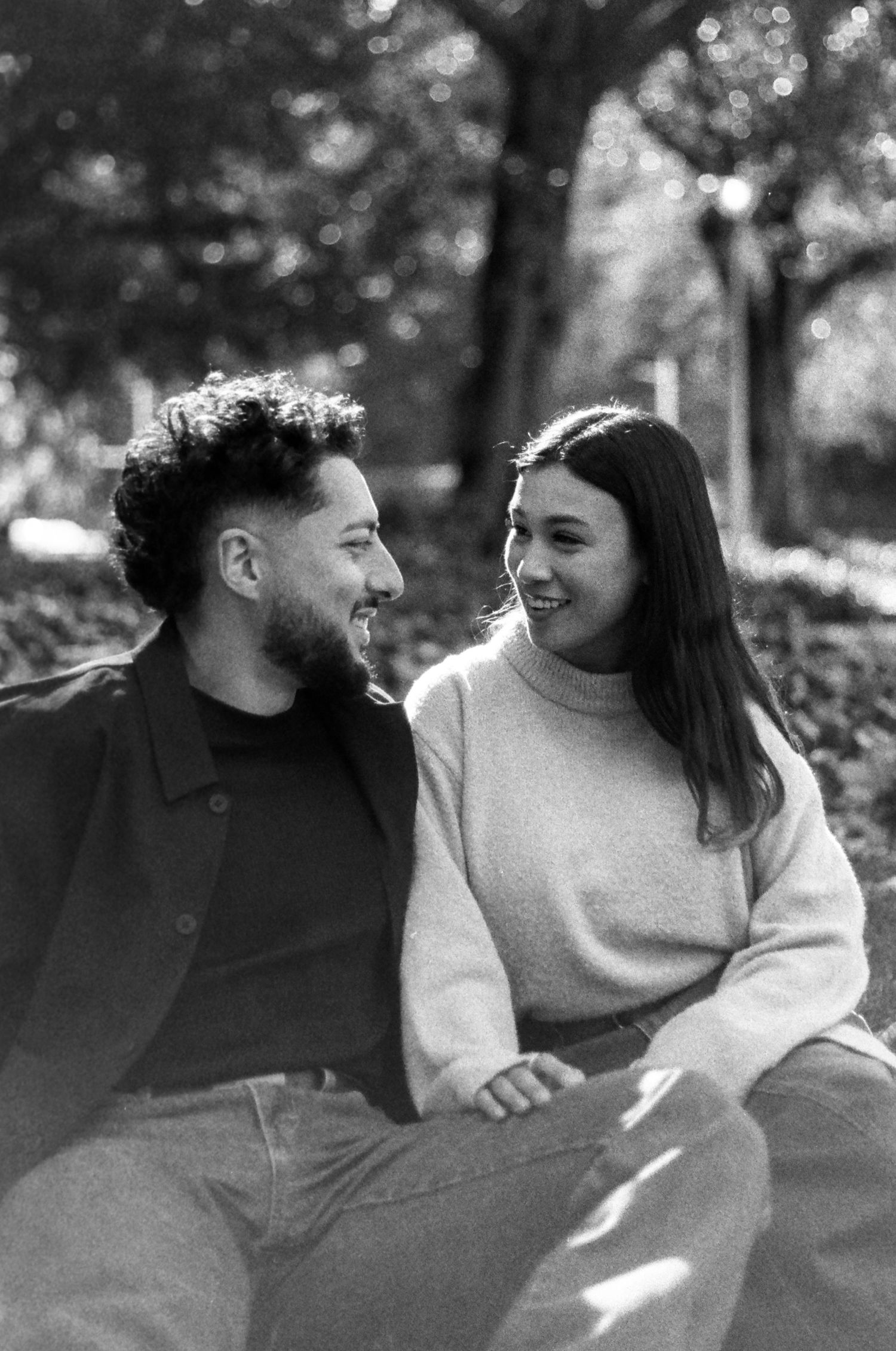 A couple in casual attire shares intimate moments while sitting together in a park setting.