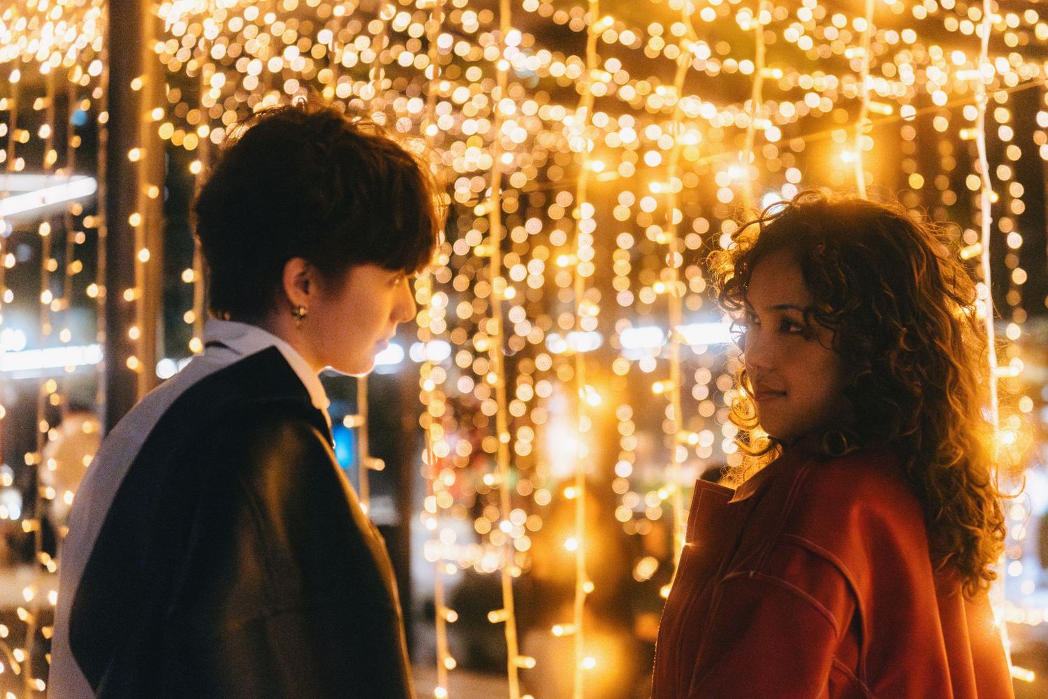 Romantic couple sits on bench under glowing string lights creating magical evening ambiance.