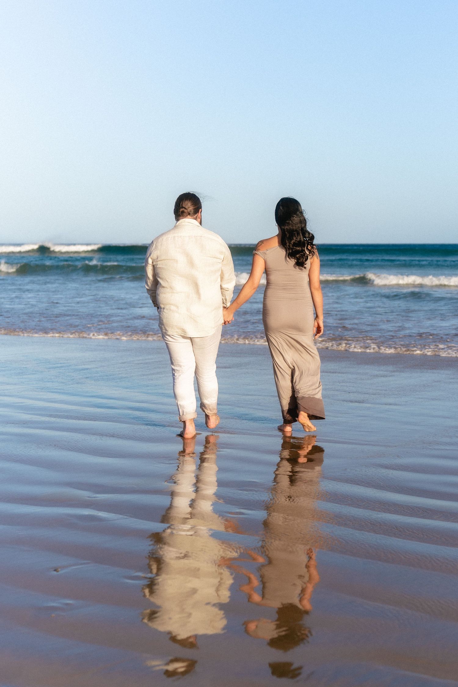 Two people walk together leaving footprints in wet beach sand.