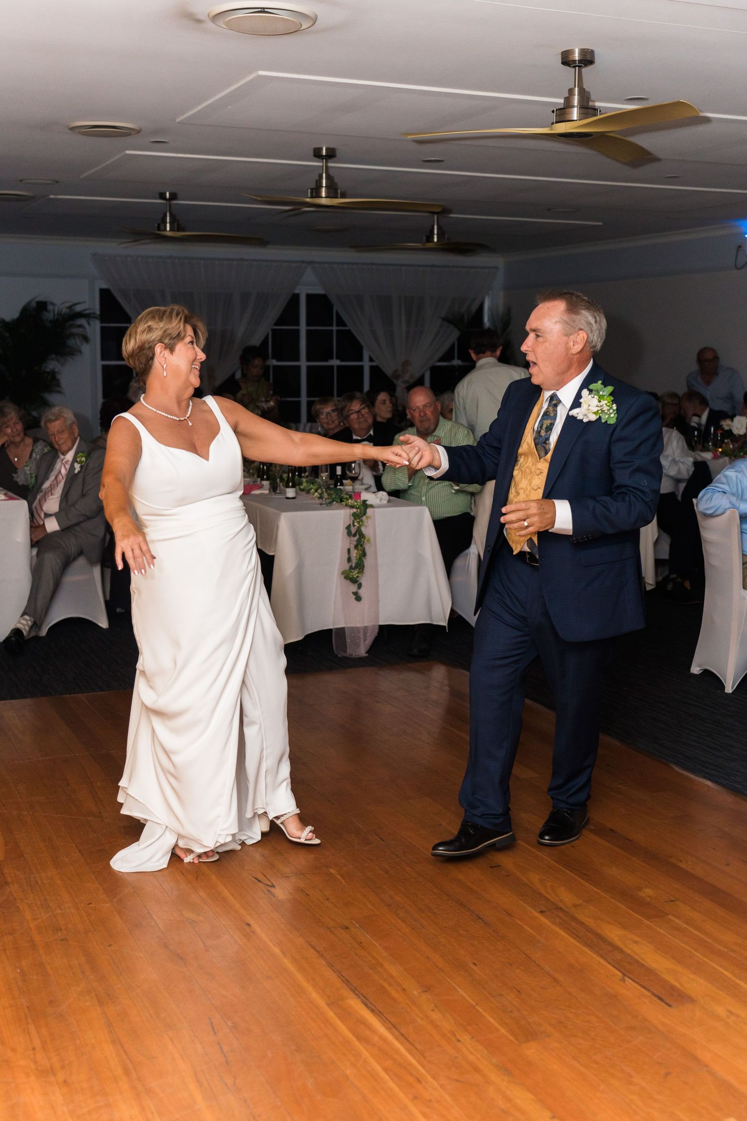 Couple dancing on wooden floor during wedding reception in decorated venue.