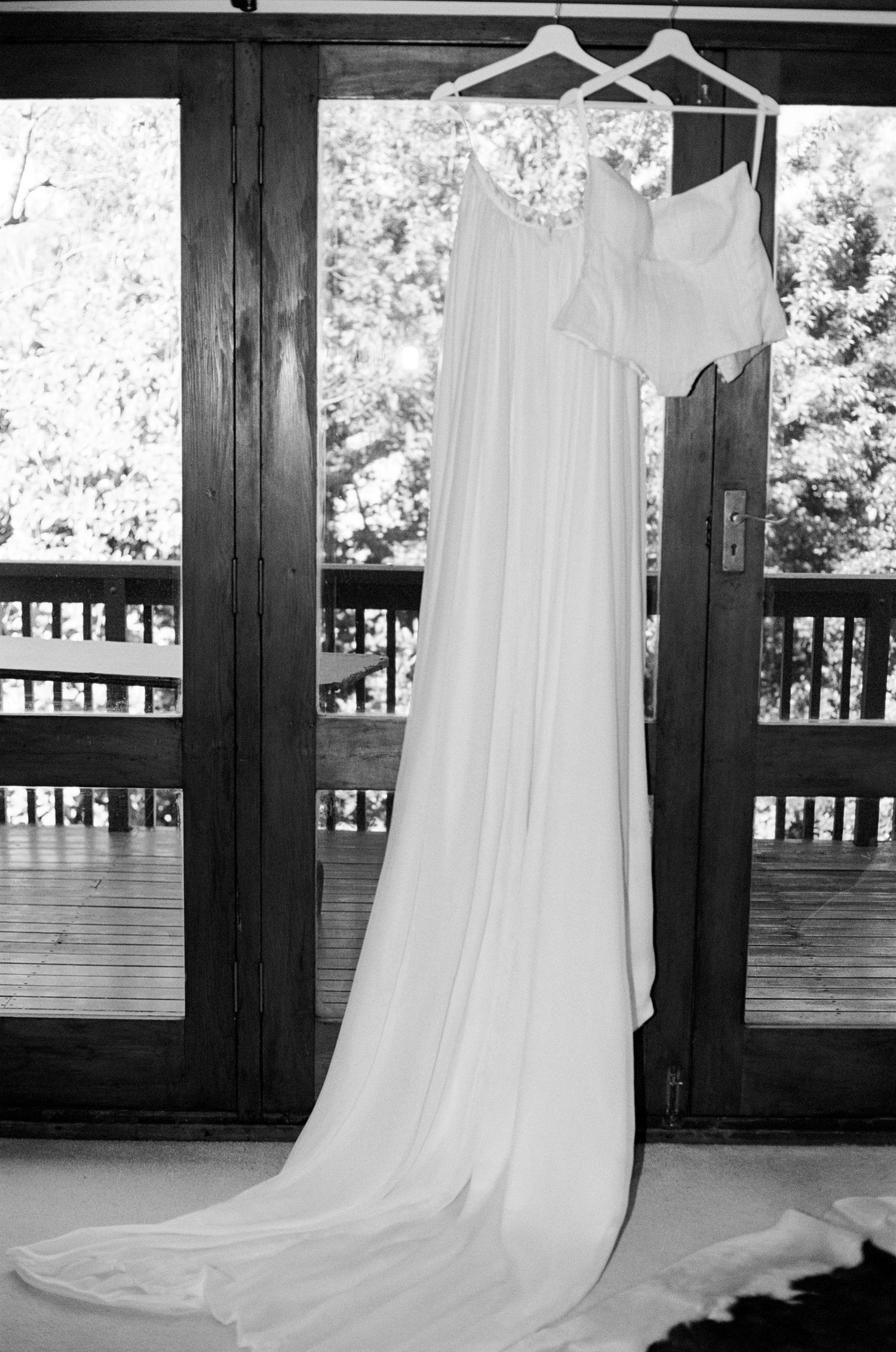 Elegant white wedding dress hanging on display against dark wooden doors with natural lighting.
