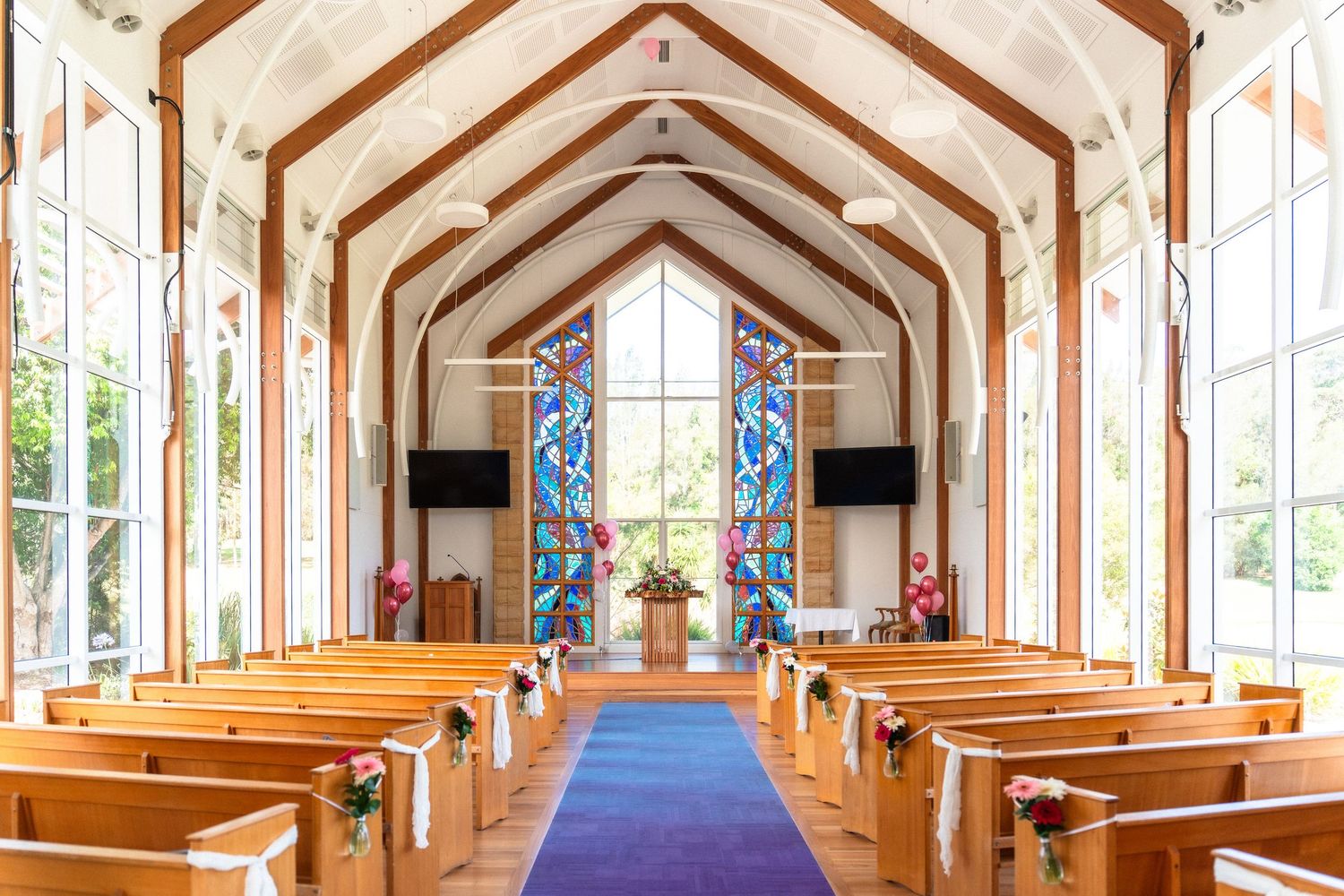 Modern church interior with vaulted ceiling, wooden pews, and stained glass windows.