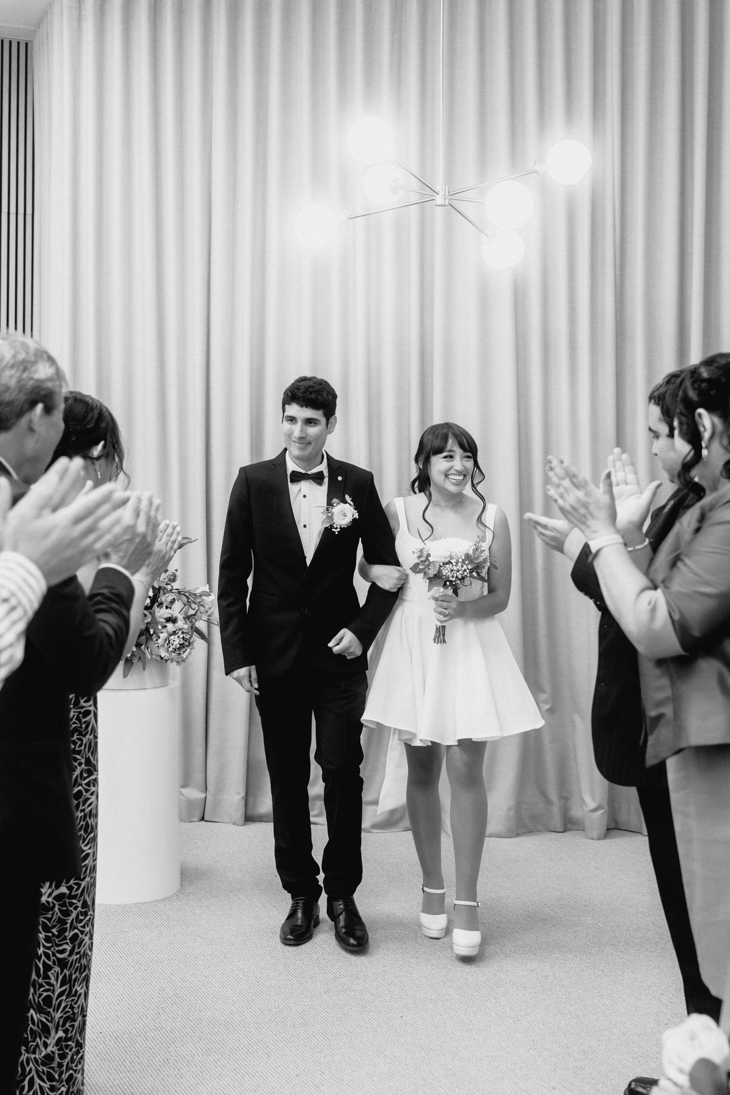 Wedding party celebrating with couple in modern venue with sage green backdrop.