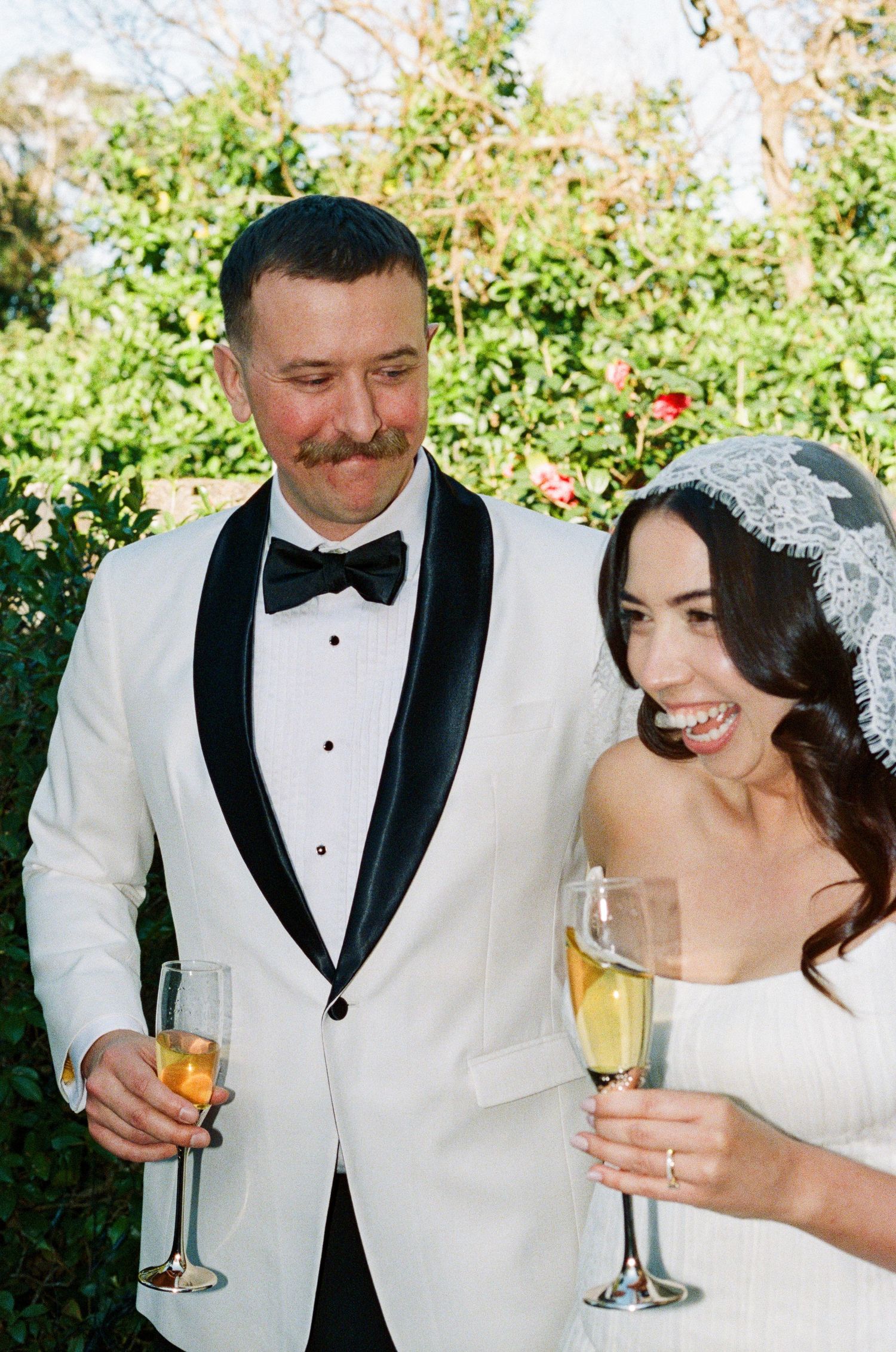 Wedding couple toasting with champagne glasses while sharing joyful moments outdoors.