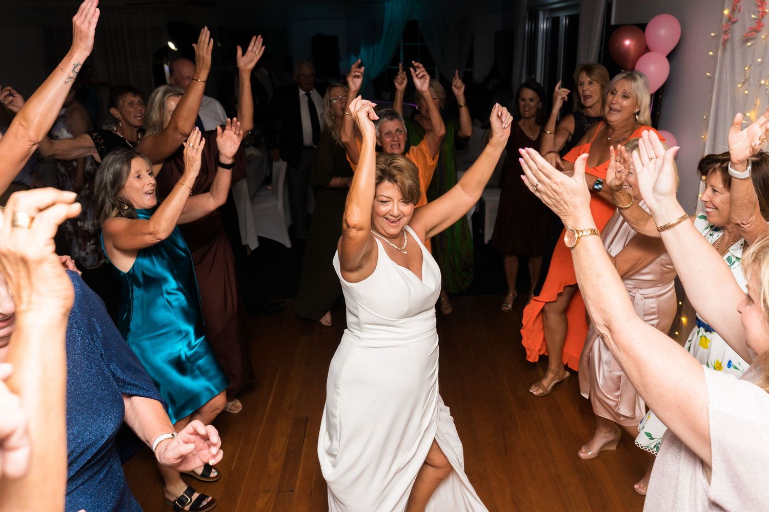 Enthusiastic wedding guests dancing with raised arms on a lively dance floor.