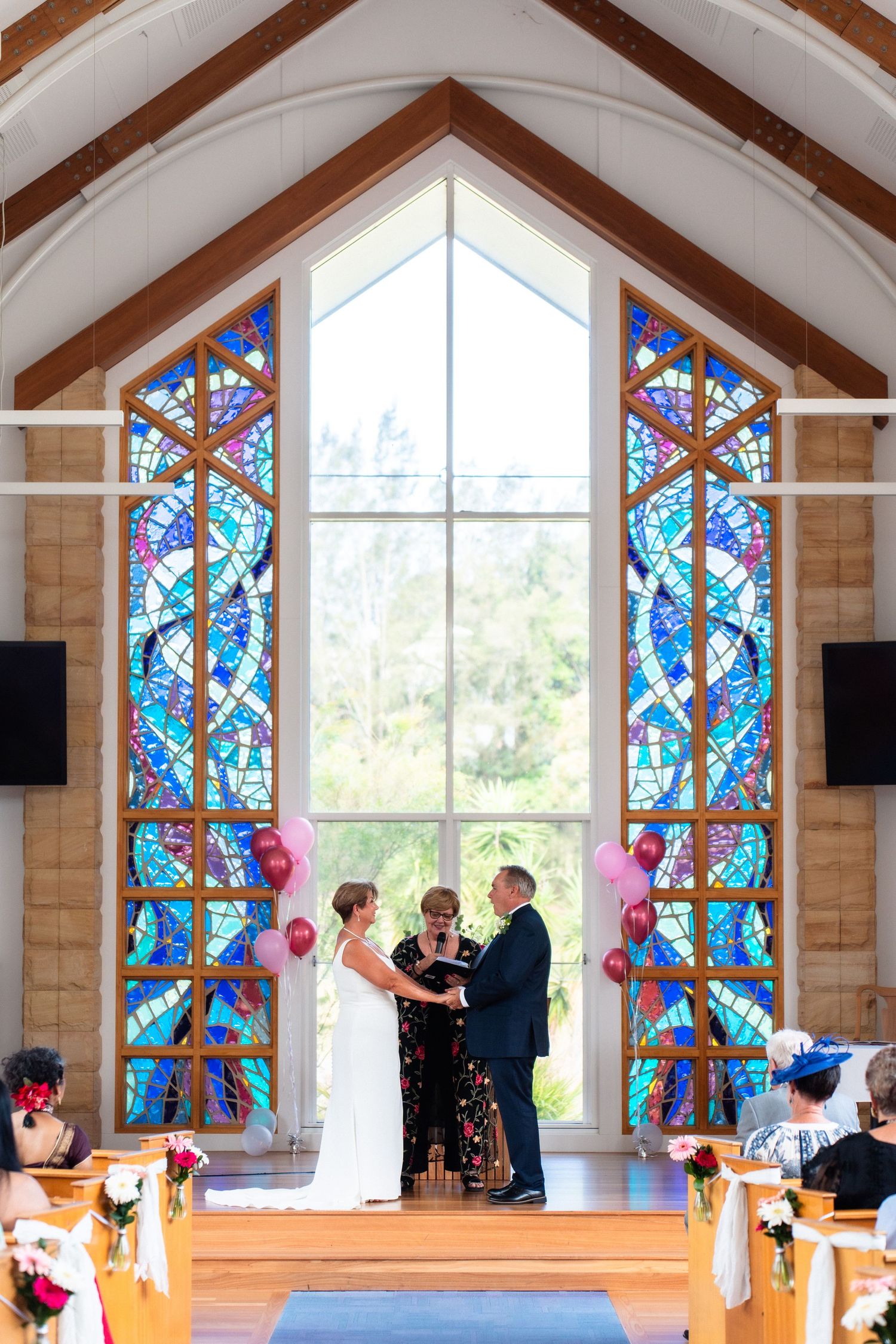 Church wedding ceremony with colorful stained glass windows and wooden pews.