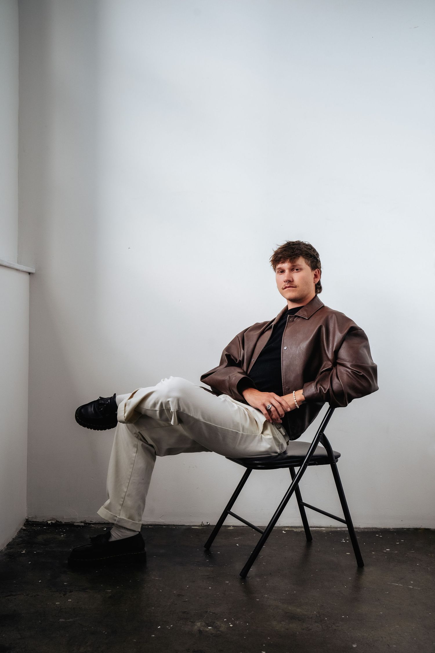 Casual portrait on folding chair wearing brown leather jacket and light pants.
