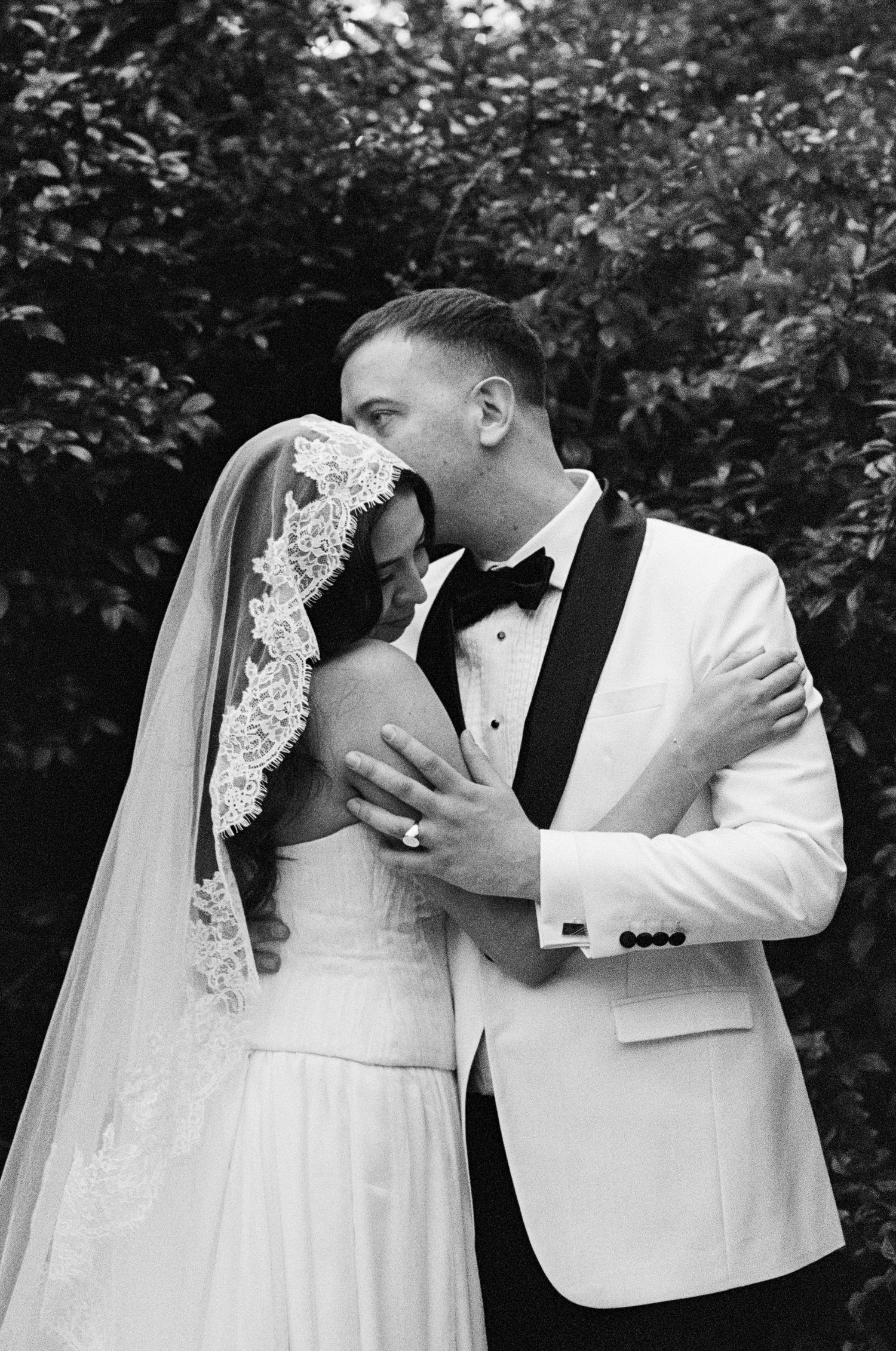 Black and white wedding portrait showing elegant formal attire and tender embrace.
